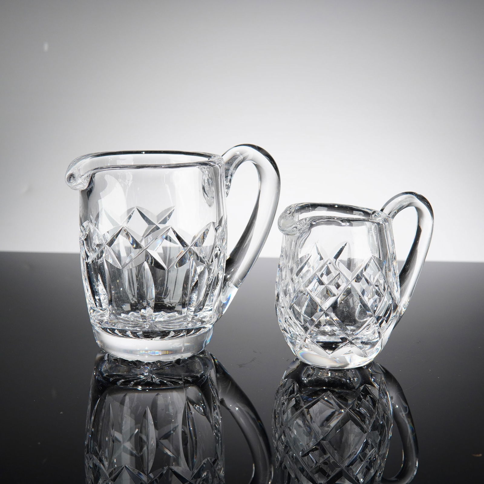 A Pair of Cut Lead Crystal Graduated Creamers, Attributed to Waterford: This pair of graduated small pitchers or creamers is crafted from high-quality lead crystal, exhibiting exceptional clarity and brilliant prismatic light refraction. The larger pitcher features a soph