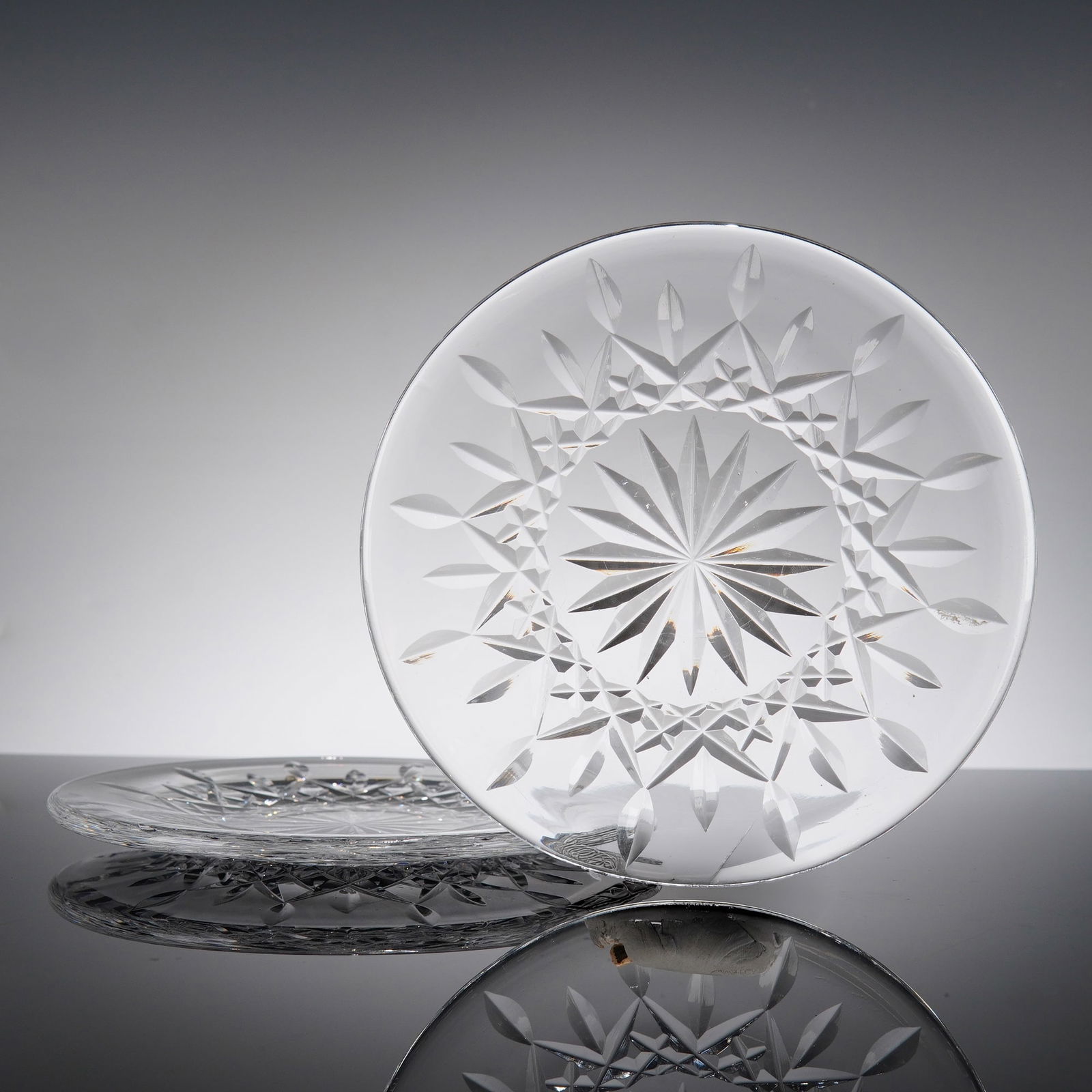 A Pair of Waterford Overture Pattern Cut Crystal Dessert Plates: This pair of circular dessert or cabinet plates is crafted from fine lead crystal, featuring an intricate and precision-cut radial design. The center of each plate is anchored by a large, multi-point