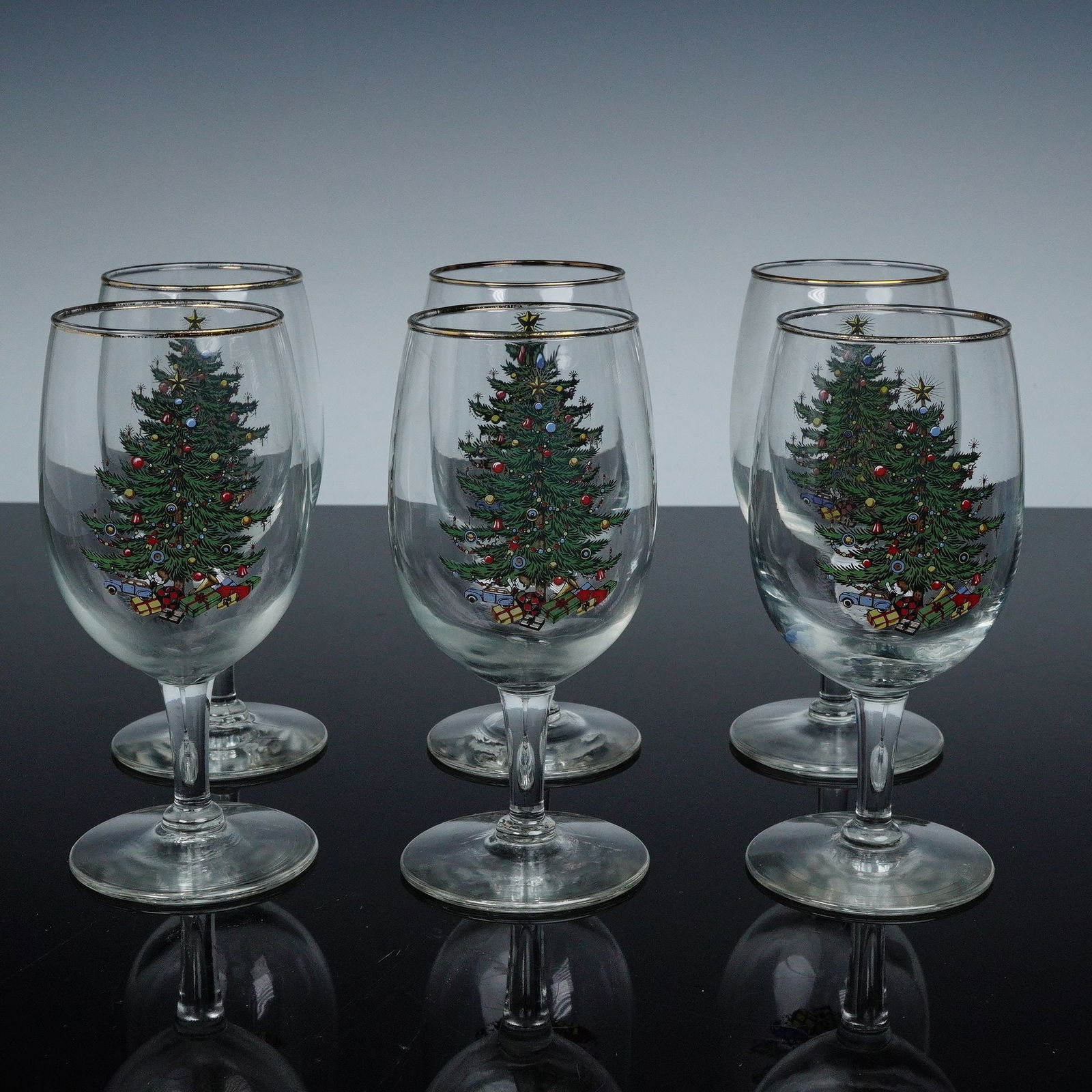 6pc Cuthbertson Wine Glasses, Christmas Tree: Each clear stemmed wine glass is decorated to the bowl with the classic Christmas Tree pattern. Depicts a festively adorned evergreen surrounded by garlands, ornaments, and wrapped gifts, the rim