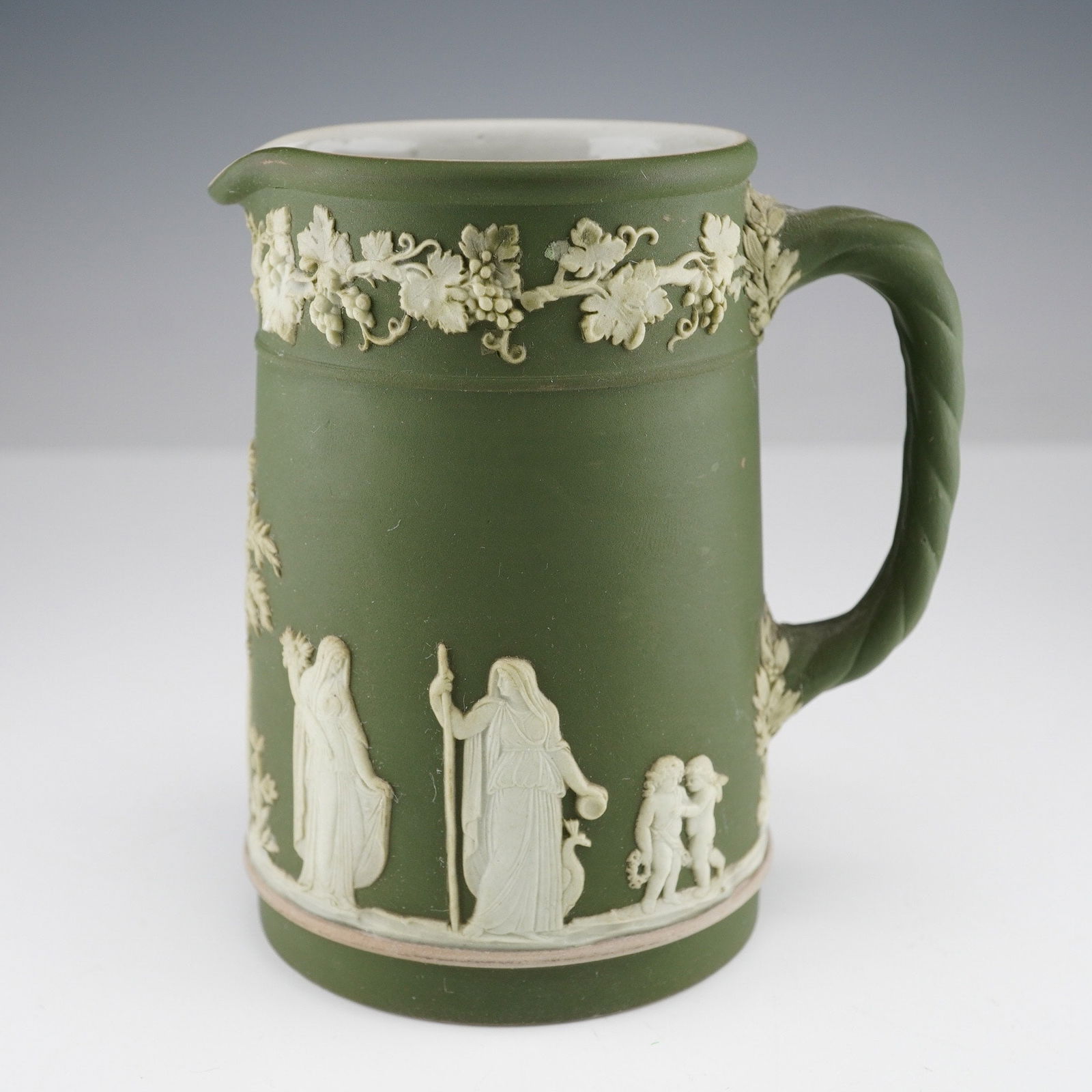 A Wedgwood Sage Green Jasperware Pitcher: A Wedgwood Sage Green Jasperware Pitcher of Neoclassical style, featuring white bas-relief decoration depicting classical figures, putti, trees, and grapevines on a matte sage-green ground. The pitche