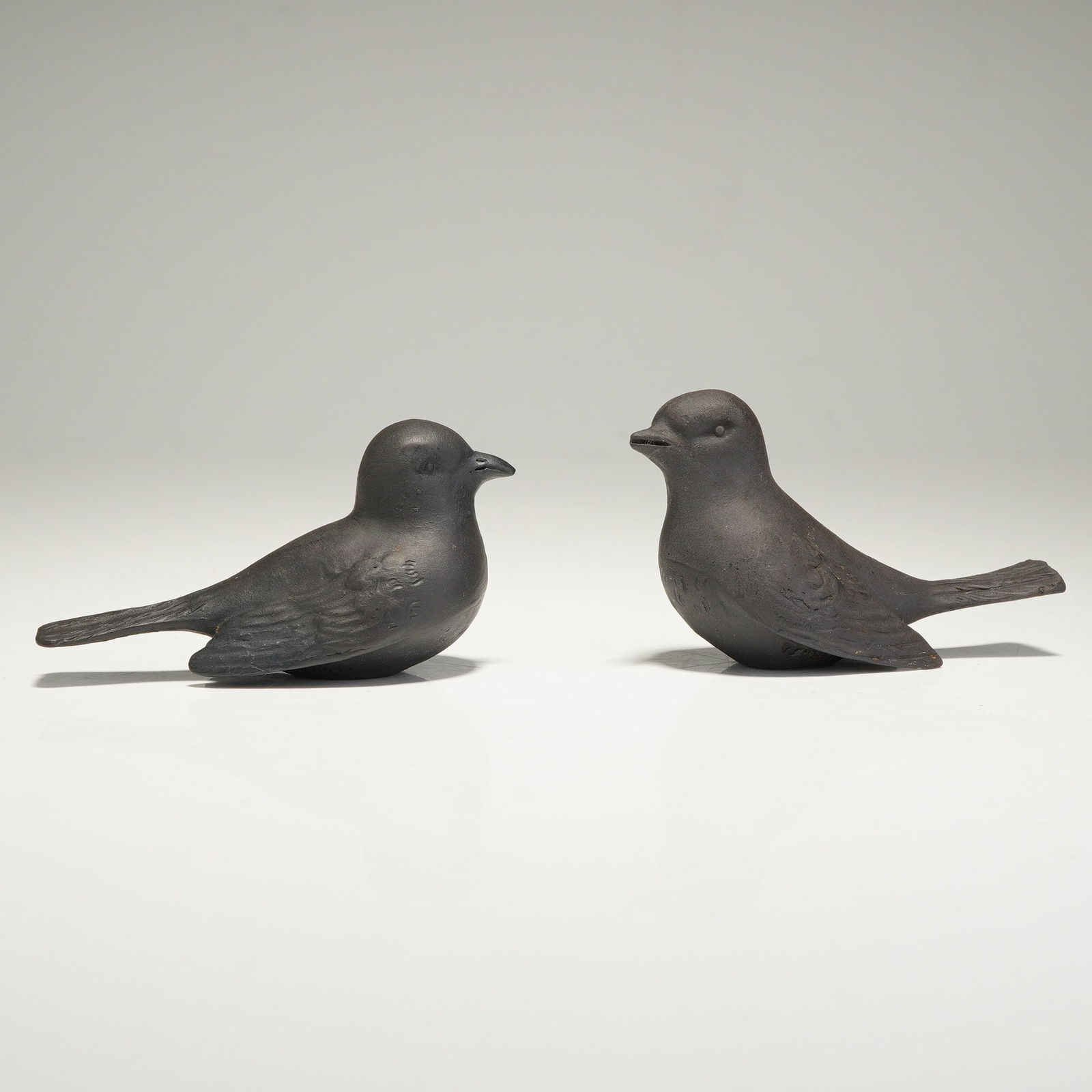 Two Wedgwood Black Basalt Bird Figurines: This two-piece set of Wedgwood bird figurines is crafted from black basalt stoneware. These pieces exhibit a matte, unglazed finish and are designed in a stylized mid-20th-century aesthetic. One figur