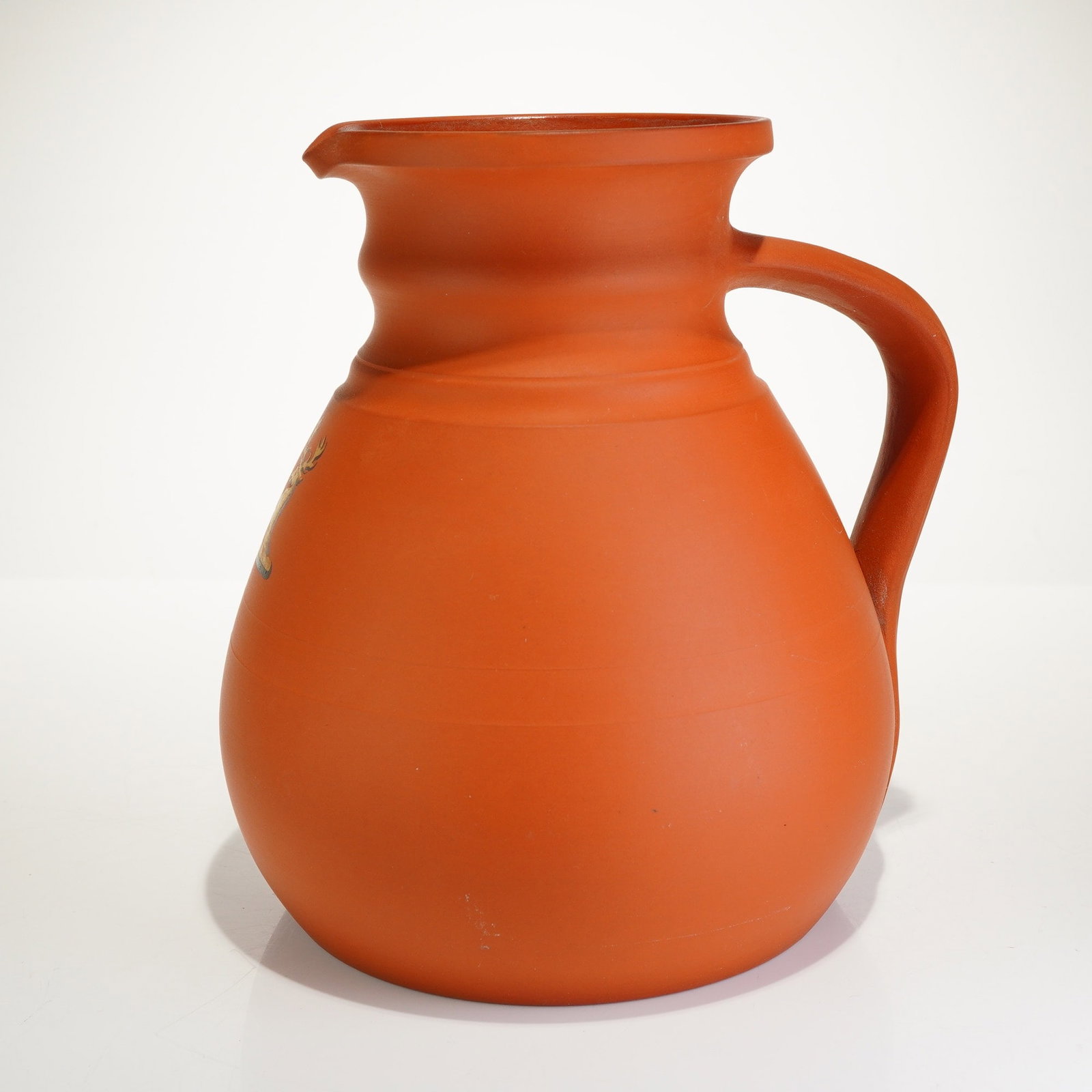Wedgwood Rosso Antico Red Ware Cambridge Ale Jug: This Wedgwood Rosso Antico red ware jug, also known as a Cambridge ale jug, is composed of unglazed, matte orange-red terracotta stoneware. The vessel is designed with a bulbous body, a waisted neck,