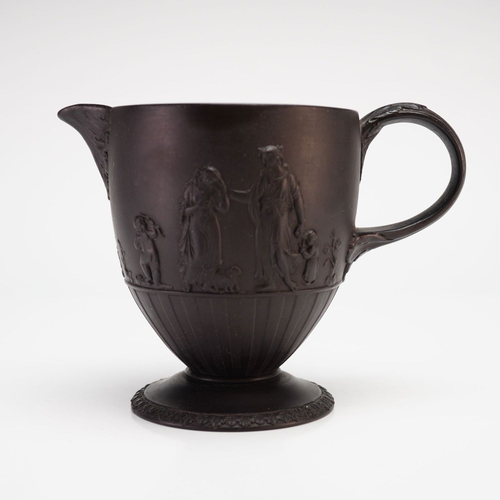 Wedgwood Black Basalt Four Home Nations Creamer: A Wedgwood black basalt creamer featuring the Four Home Nations pattern in Neoclassical bas-relief. The vessel is constructed with a footed base, a fluted lower body, and a decorative handle with foli