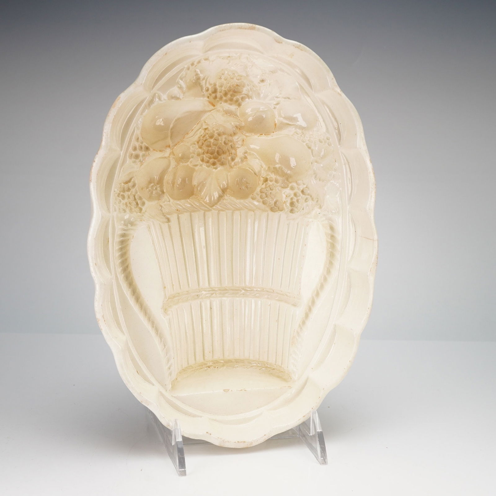 Wedgwood Creamware Oval Jelly Mold: A Wedgwood creamware pottery mold of oval form featuring a scalloped rim and a deeply molded interior. The central design depicts a basket filled with assorted fruits, including grapes, pears, and ber
