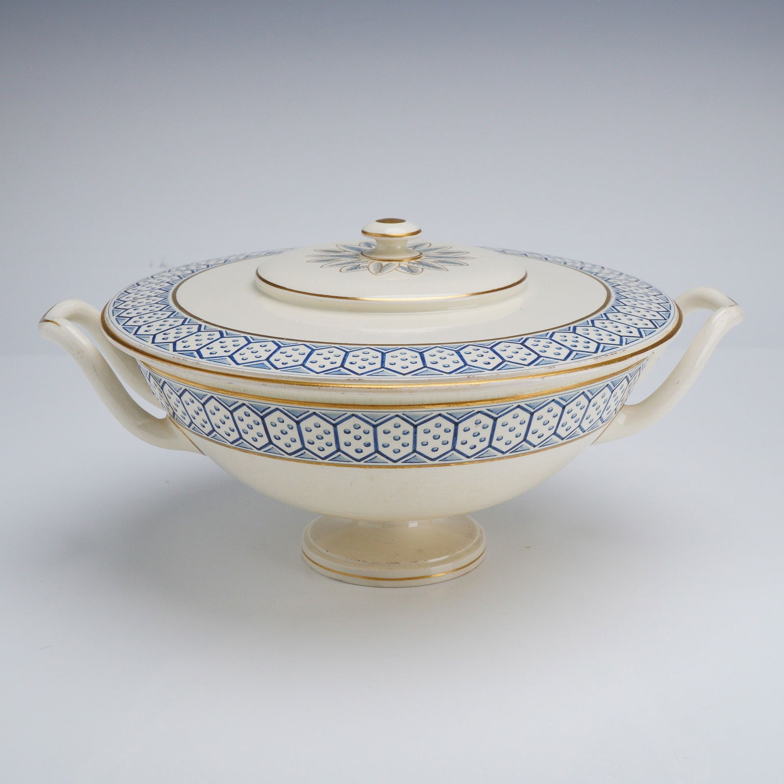 Wedgwood Creamware Covered Bowl: A Wedgwood creamware covered bowl featuring a characteristic off-white glaze. The vessel is decorated with a repeating blue geometric border of hexagonal cells containing dotted patterns, elegantly ac
