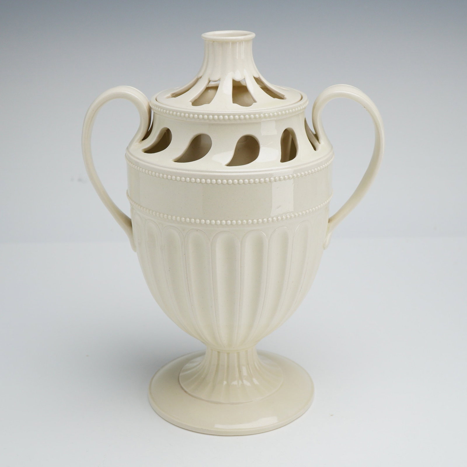 Wedgwood Neoclassical Creamware Two-Piece Reticulated Potpourri Urn: A fine Wedgwood creamware potpourri urn and flower frog insert designed in the Neoclassical taste. This two-piece set is crafted from cream-colored glazed earthenware, featuring a twin-handled urn sup