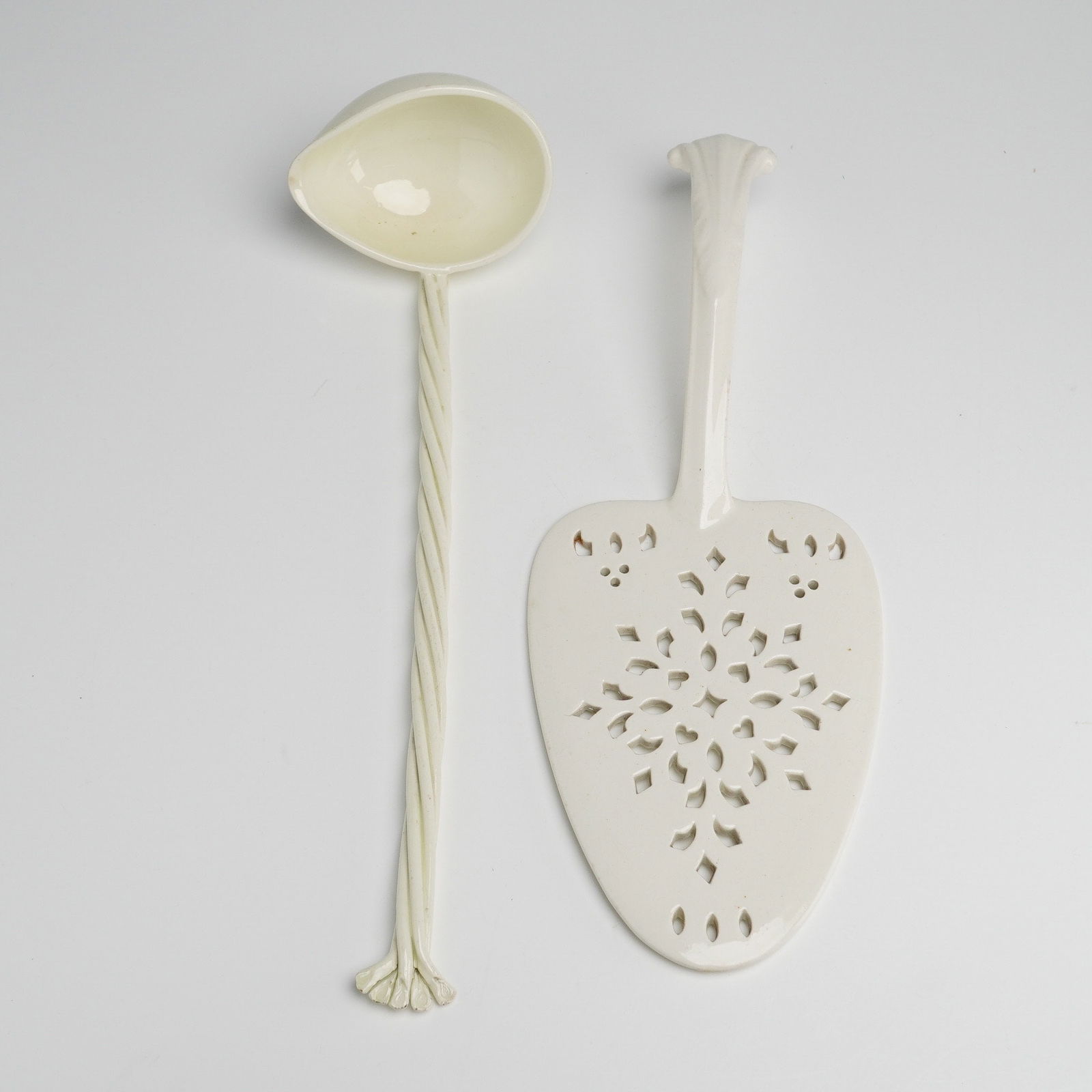 A 2pc Wedgwood Creamware Fish Slice and Ladle: A 2pc Wedgwood creamware serving set comprising a fish slice and a ladle. The fish slice features a reticulated blade with an intricate pierced geometric pattern and a faceted, curved handle. The ladl