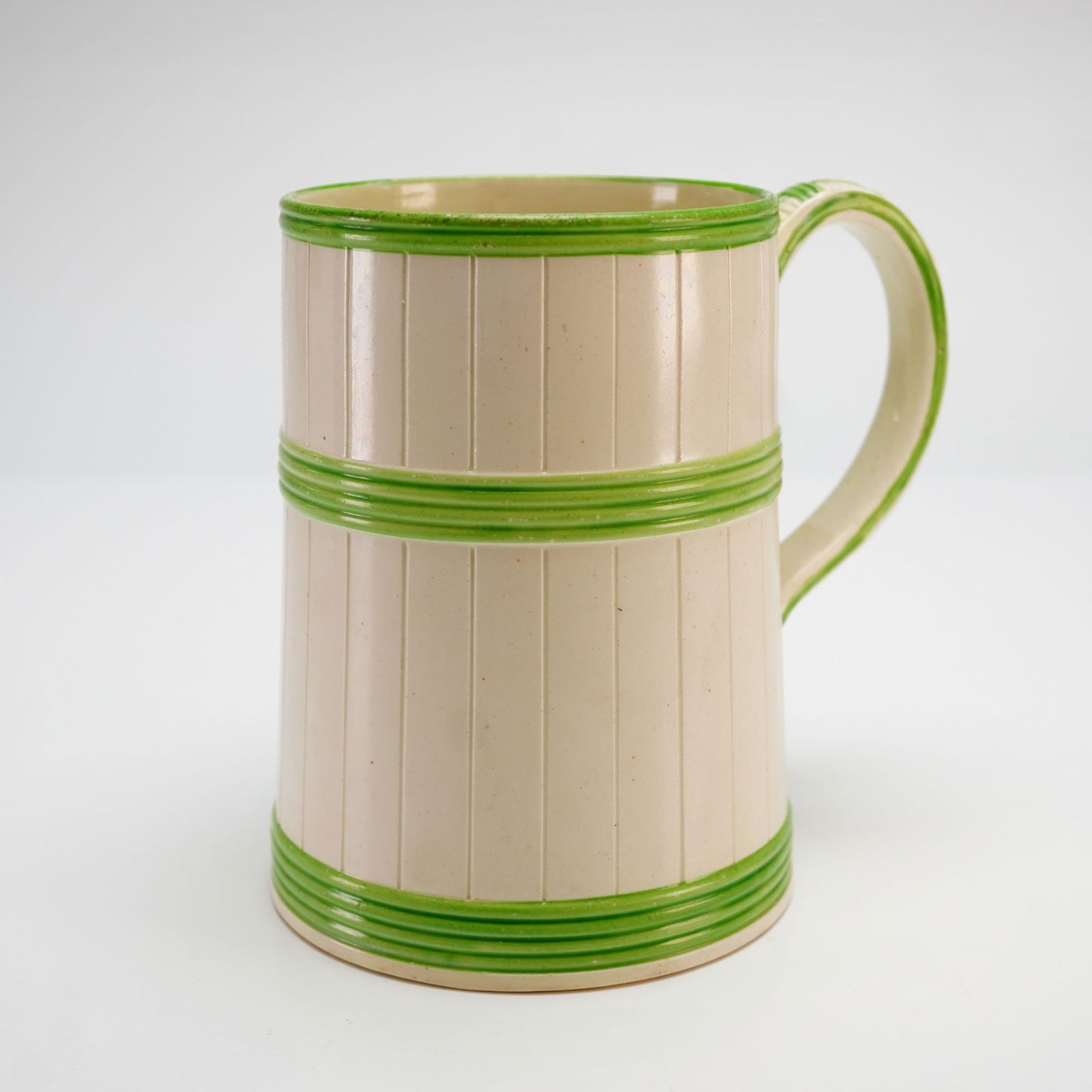 Wedgwood Green-Glazed Reeded Creamware Porter Tankard Mug: This early 19th-century Wedgwood cream ware mug is a fine example of a porter tankard featuring a classic creamware body and a slightly tapering cylindrical form. The exterior is decorated with vertic