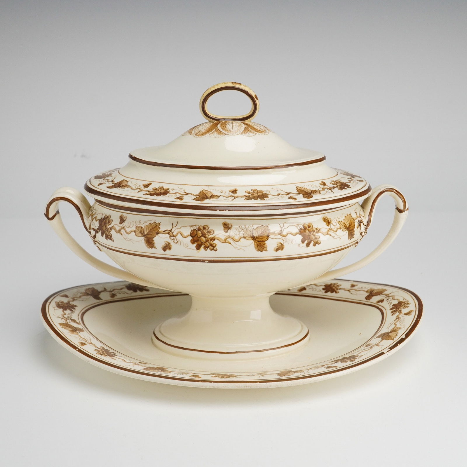 Wedgwood Etruria Creamware Footed Tureen with attached Underplate: A trio of Wedgwood of Etruria creamware ceramic items featuring a footed tureen with attached underplate and a fitted lid. Crafted from cream-toned glazed earthenware, the pieces are decorated with br