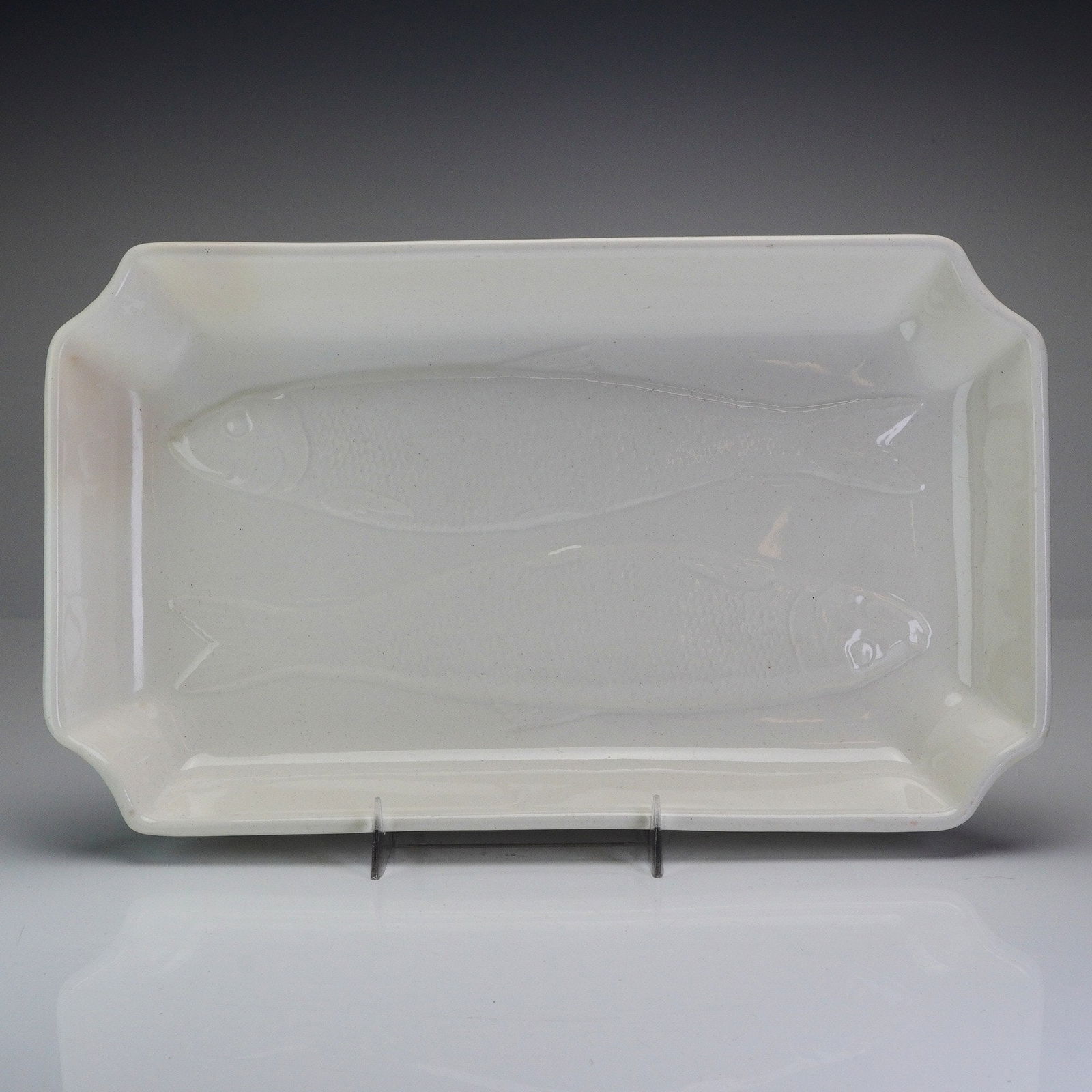 Wedgwood Queensware Herring Serving Dish: This rectangular creamware serving platter features a shallow well with notched corners and a low-relief molded decoration of two fish in the central well. The vessel is finished in a uniform creamy w