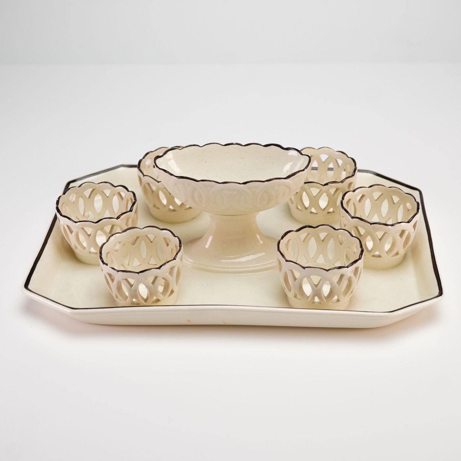 Wedgwood Creamware Tray with Seven Attached Cups: This Wedgwood porcelain tray with seven attached cups is crafted from cream-glazed ceramic, commonly referred to as creamware. The set is composed of a rectangular tray with angled corners that holds