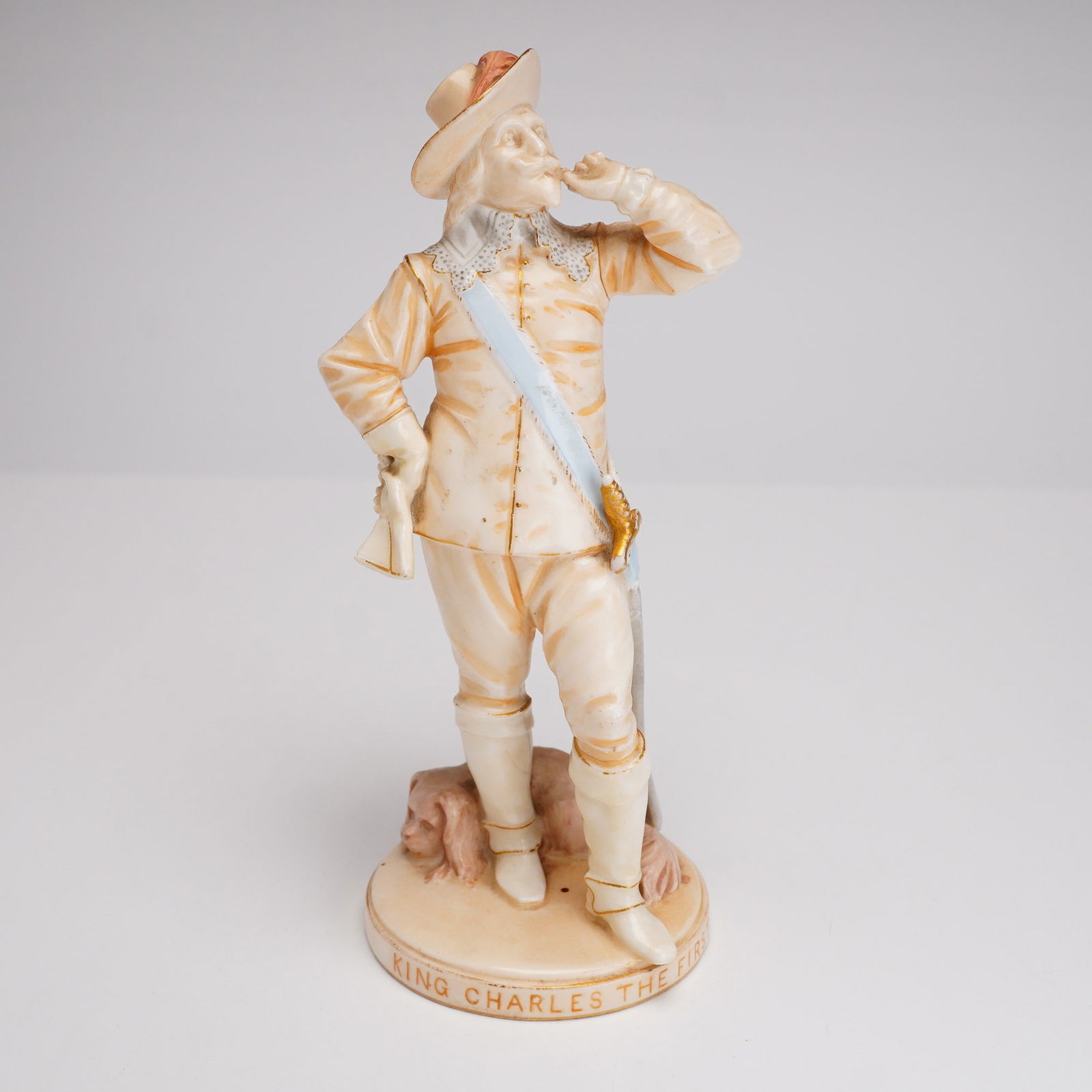 Wedgwood King Charles I Porcelain Figurine: A Wedgwood tinted bisque porcelain figurine of King Charles I, likely modeled after the famous portrait by Sir Anthony van Dyck. The King is depicted in 17th-century courtly attire, including a feathe