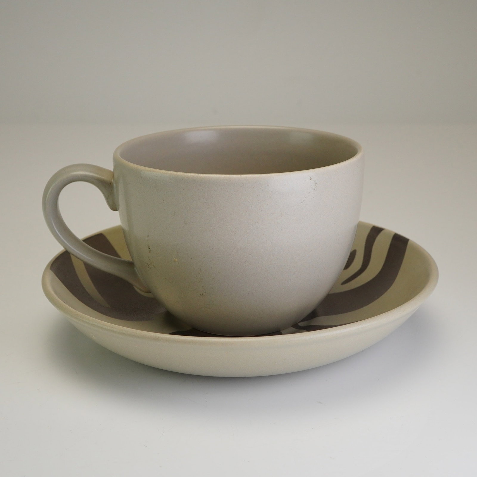 2pc Nigel Coates Wedgwood Cup and Saucer Set: This contemporary ceramic cup and saucer set was designed by Nigel Coates for the Wedgwood. The set features a matte greige glaze accented with dark gray abstract, organic motifs. The saucer is decora