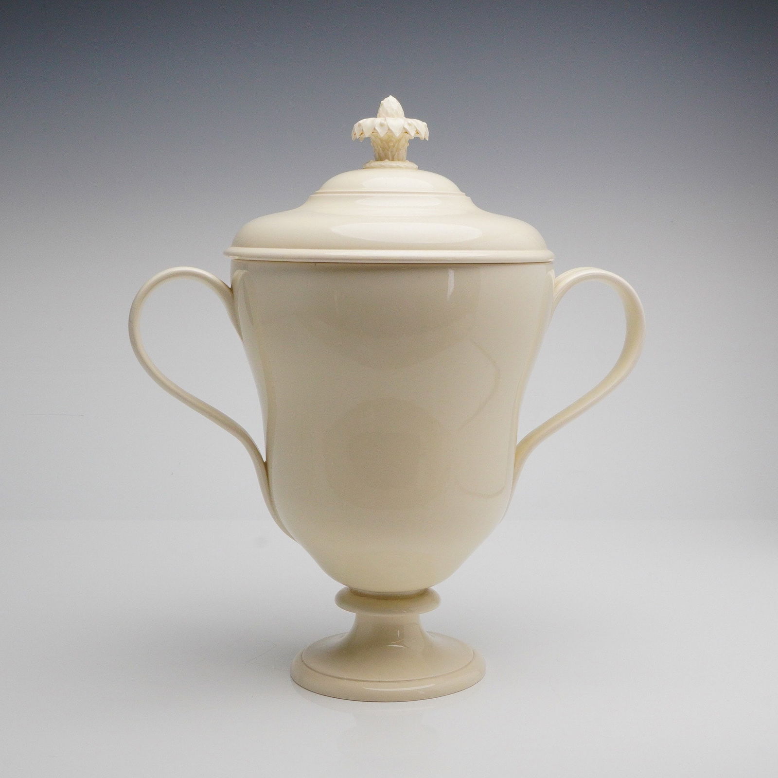 Wedgwood Etruria Covered Urn with Pinecone Finial: A single covered urn manufactured by Wedgwood, executed in pale cream-colored glazed ceramic. The vessel is modeled in a Neoclassical revival style, featuring a deep, waisted body resting on a flared
