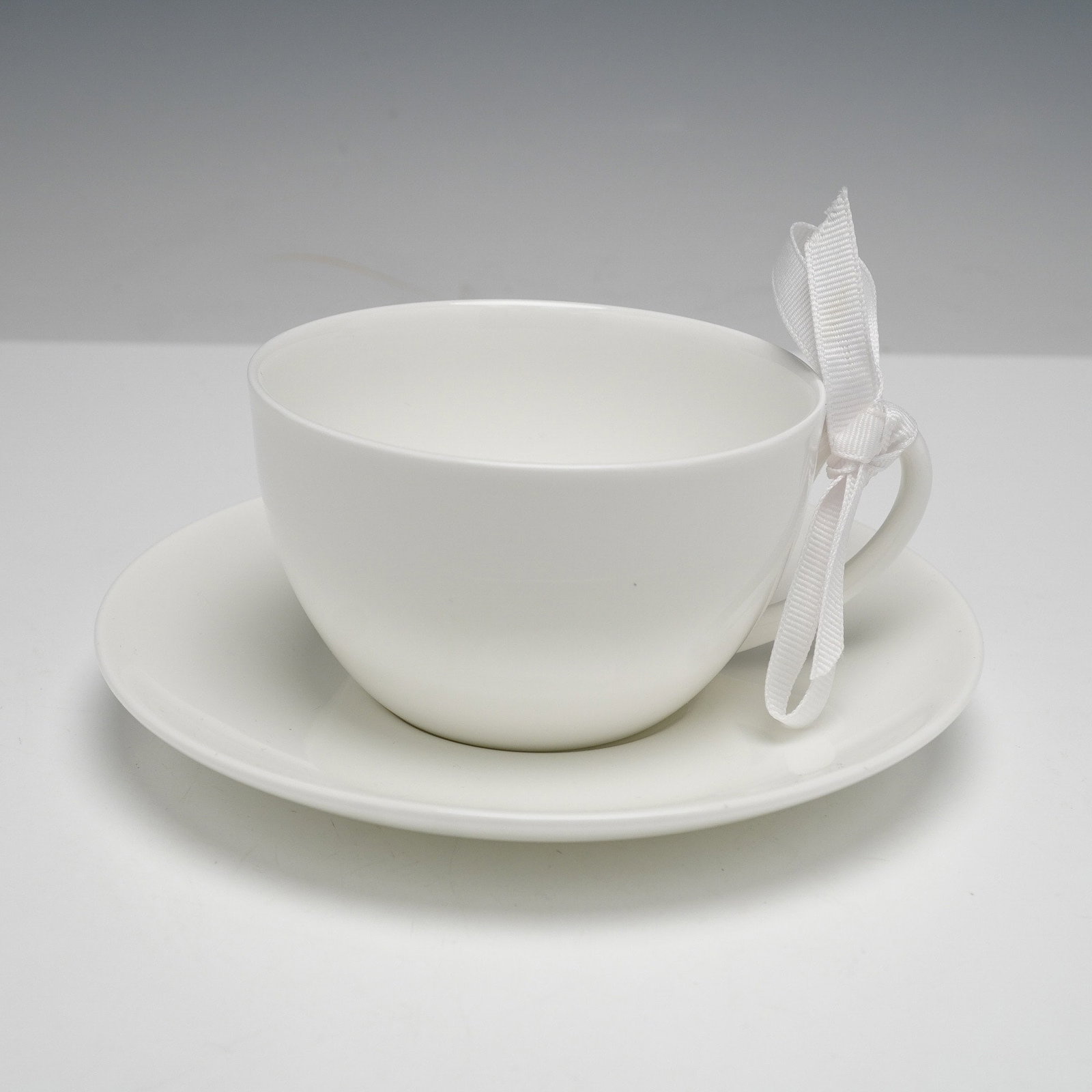 A Wedgwood 'Eternity' English Bone China Teacup and Saucer Set: A contemporary English bone china teacup and saucer set by Wedgwood, in the 'Eternity' pattern with a W stamped on the saucer . Both pieces are unadorned and feature a minimalist white design. The und