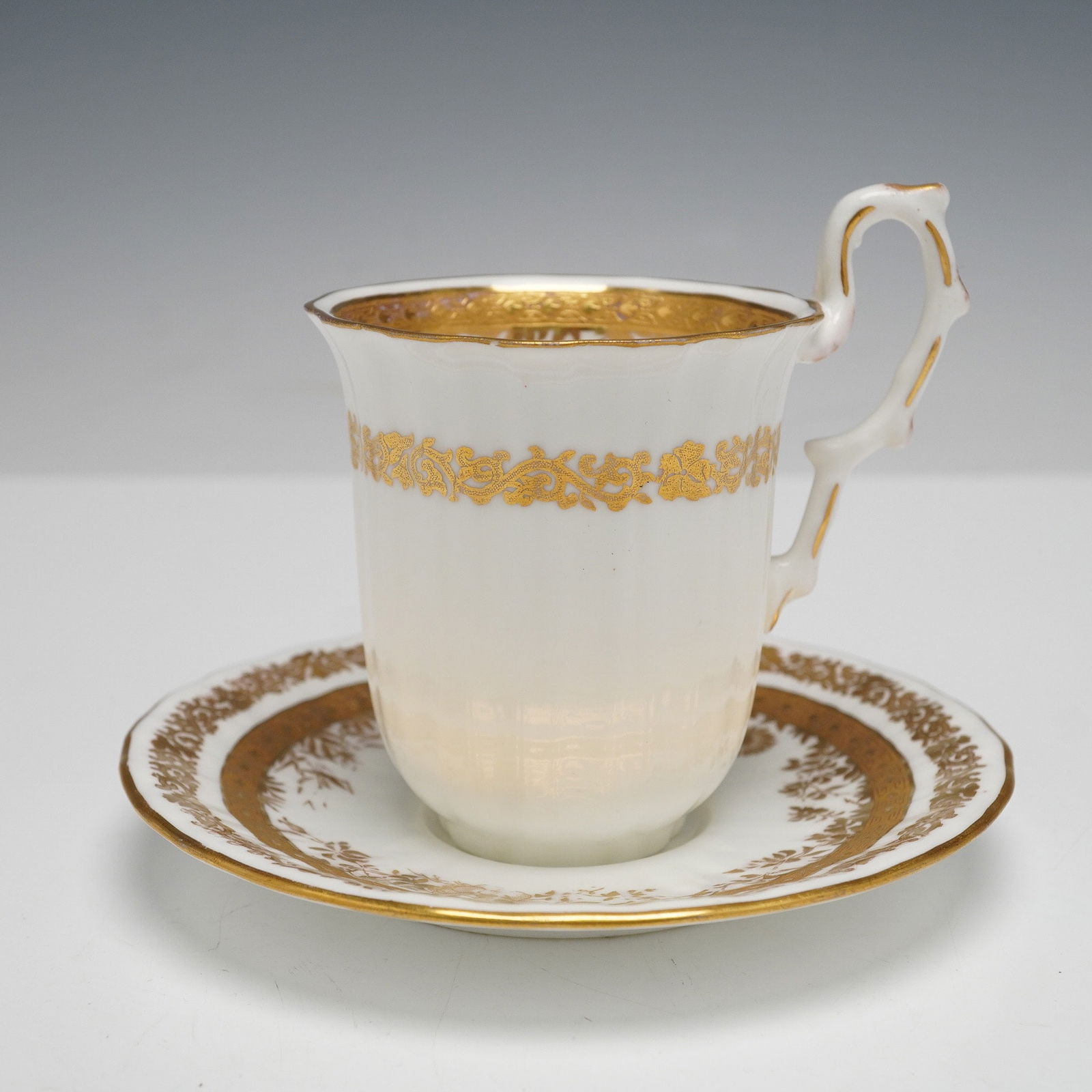 A Wedgwood Gilt-Decorated Bone China Teacup and Saucer: A rare Wedgwood teacup and saucer set, circa 1910, crafted from bone China, extensively decorated with gold gilding. The cup features a gilt scroll-patterned band and a distinctive branching handle. T