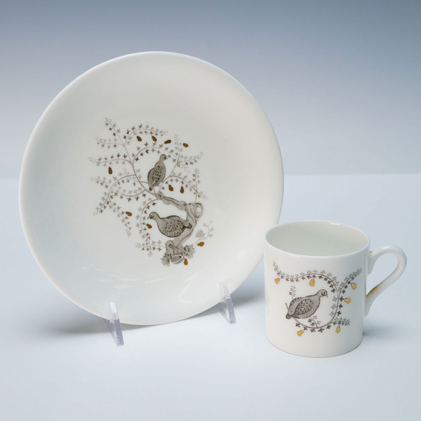A Wedgwood 'Partridge In A Pear Tree' Bone China Cup and Saucer Set: A Wedgwood 'Partridge In A Pear Tree' cup and saucer set, crafted from bone china. Both pieces feature a stylized naturalistic motif depicting one or two grey and brown partridge-like birds nestled am