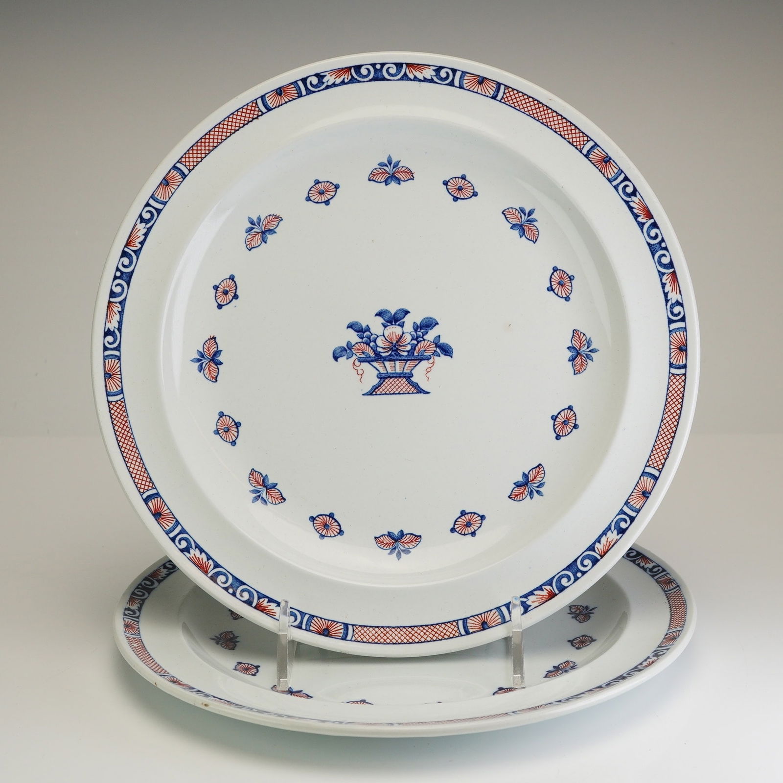 A Pair of Wedgwood Vieux Rouen Dinner Plates: A pair of Wedgwood earthenware dinner plates in the Vieux Rouen pattern, produced in Etruria, England. Each plate features a central transfer-printed flower basket motif in blue and iron-red on a whit