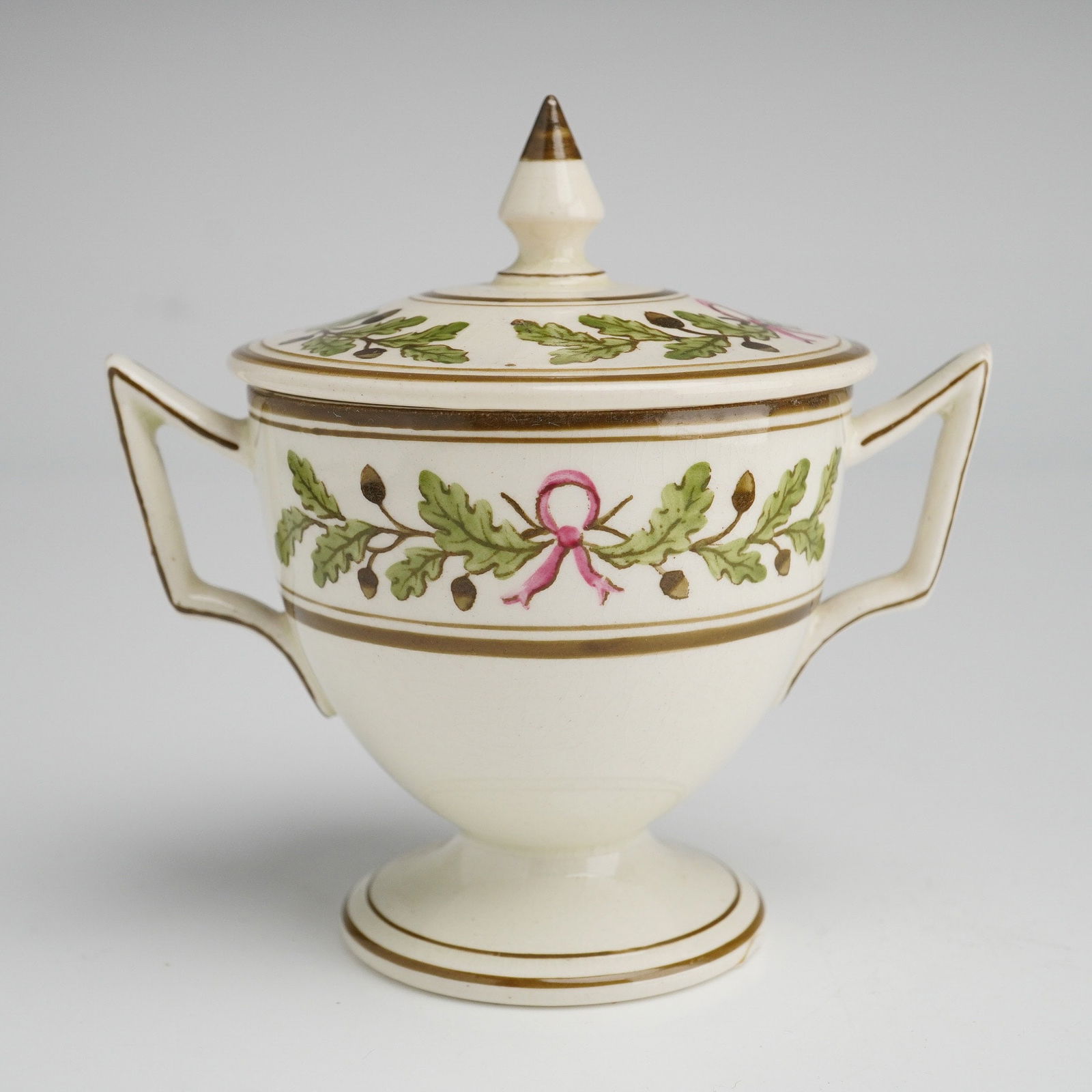 Wedgwood Footed Double Handled Lidded Sugar Bowl for James Powell and Sons: A Wedgwood creamware footed double handled lidded sugar bowl manufactured for James Powell and Sons. The vessel features a pedestal base and a body with twin angular handles, accompanied by a matching