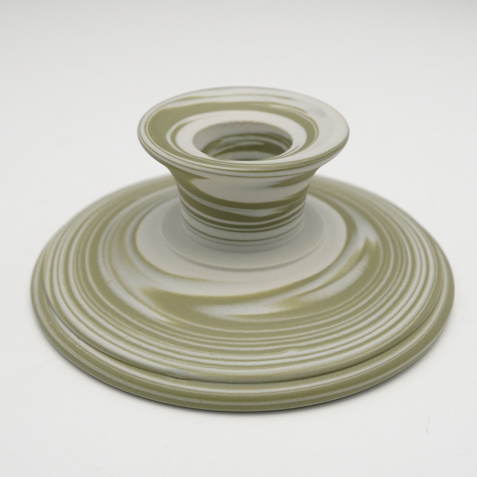 A Wedgwood Marbled Ceramic Candle Holder: A Wedgwood marbled ceramic candle holder, featuring a wide, circular foot and a central socket. The piece displays a distinctive marbled or agateware style, blending a matte pale green/sage color with