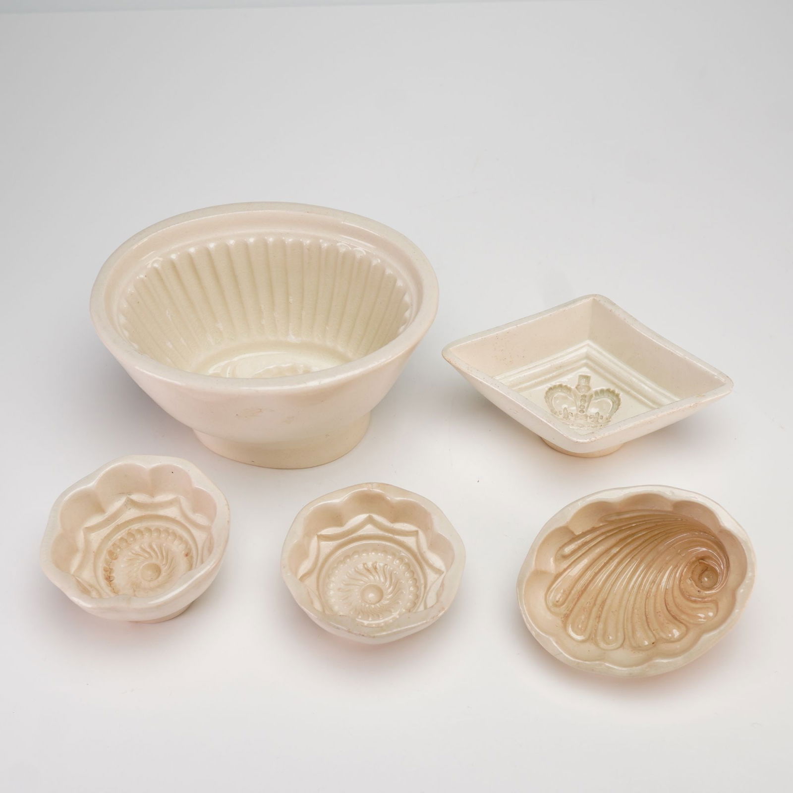 5 Wedgwood and Unmarked Glazed Stoneware Jelly Molds: A group of five glazed stoneware jelly molds, including examples by Wedgwood and unmarked pieces. The collection features a variety of forms: a large oval mold with fluted sides and a central pineappl