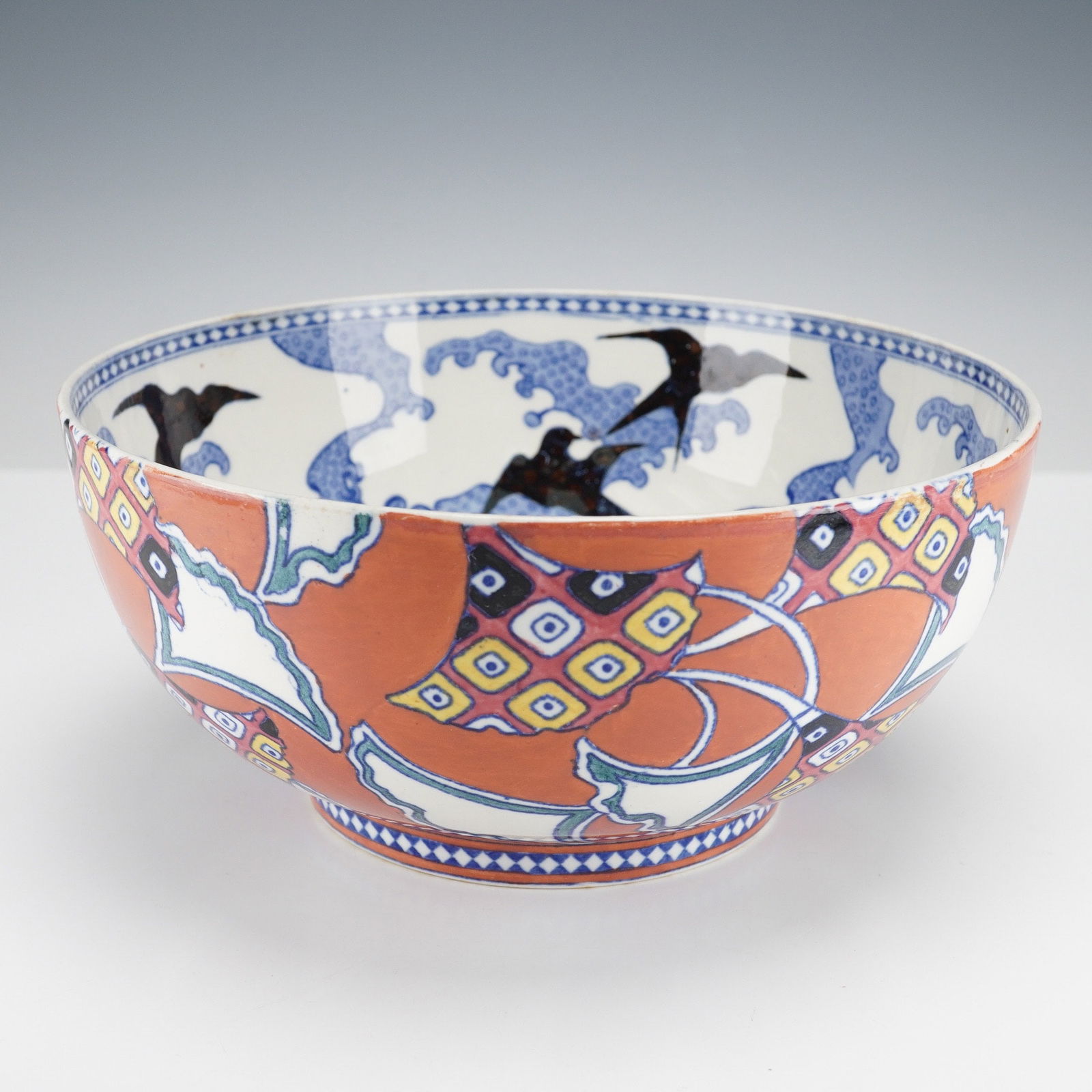 Wedgwood Porcelain Japonesque Bowl: The interior is adorned with black swallows flying amidst stylized blue waves and a central medallion echoing this motif, all executed in underglaze blue. The exterior features a terracotta-red ground