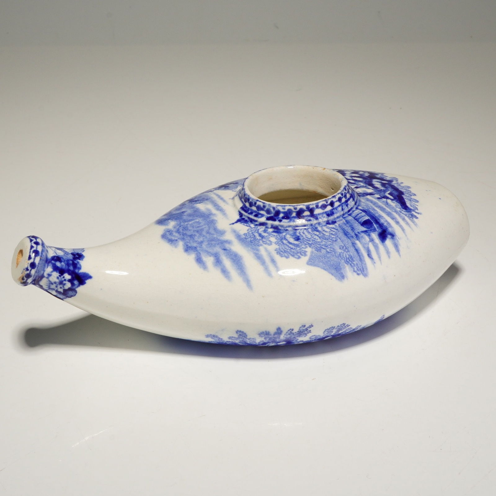 A Wedgwood Blue and White Transfer-Printed Ceramic Feeding Bottle: This 19th-century ceramic feeding bottle, attributed to Wedgwood, features an elongated and tapered form designed for use as an infant or invalid feeder. The piece is finished in a white glaze and dec