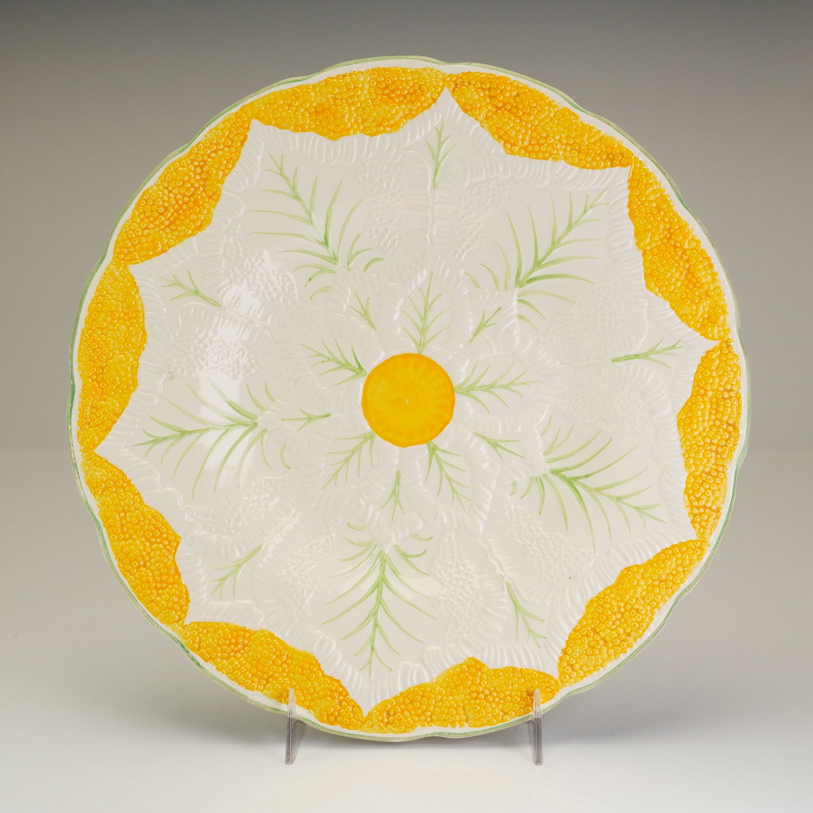 Wedgwood Etruria Majolica Cauliflower Pattern Plate: A Wedgwood earthenware majolica plate featuring a scalloped rim and relief-molded botanical leaf patterns under a clear glaze. The hand-painted decoration consists of a central yellow boss with radiat