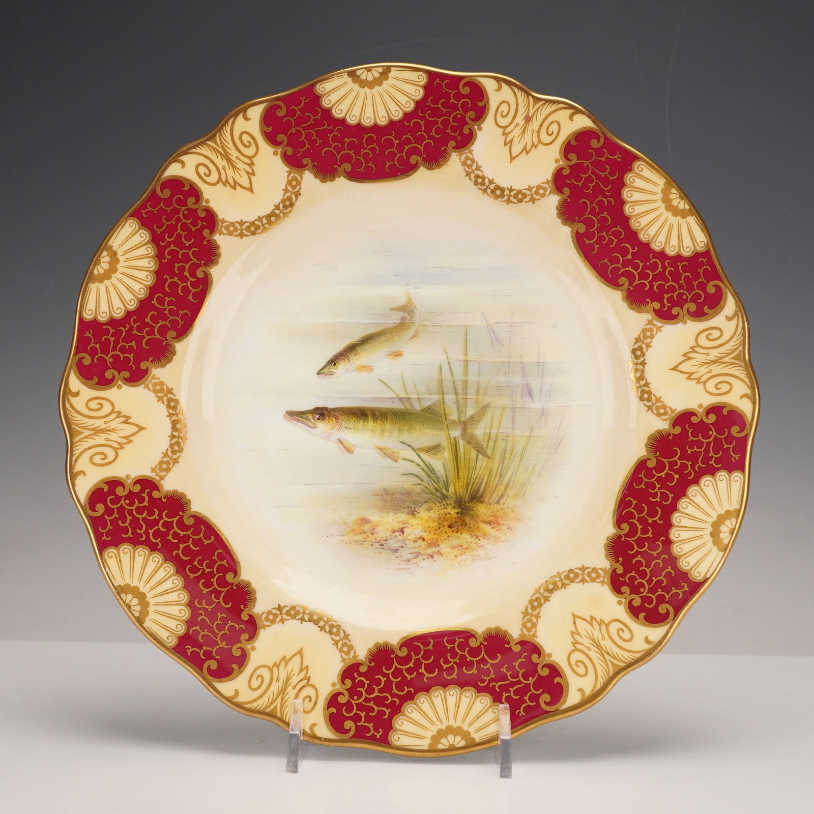 Wedgwood for T. Goode & Co. by Arthur Holland Fish Plate, Pike: A porcelain plate manufactured by Wedgwood and retailed by T. Goode & Co. Ltd., London. The plate has a scalloped gilt rim and a central hand-painted vignette depicting two pike in a freshwater settin