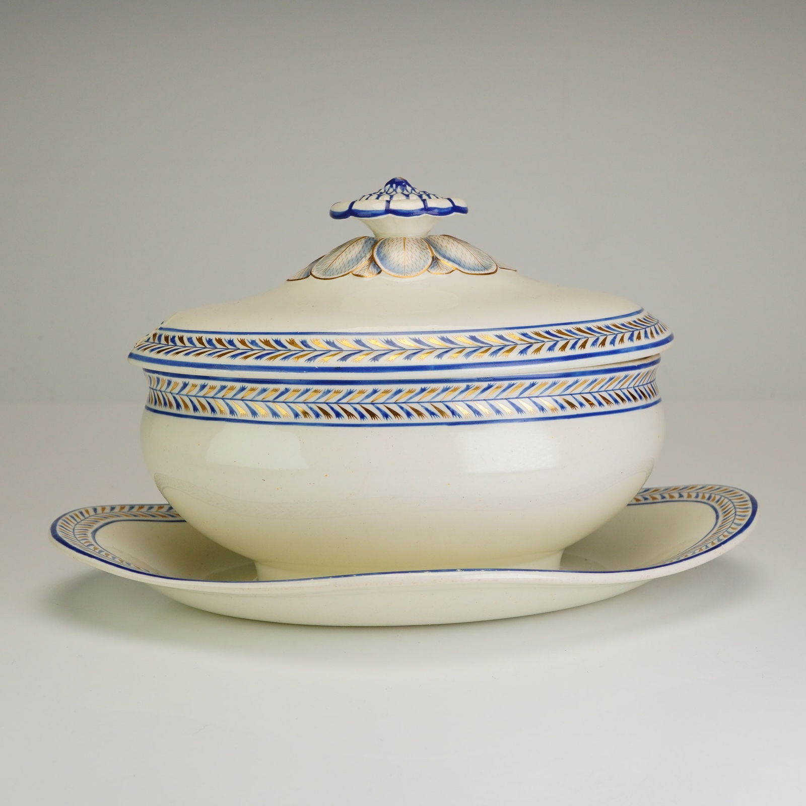 Wedgwood Gravy Boat with Attached Underplate & Lid: This Wedgwood creamware gravy boat with attached underplate and lid is executed in the Neoclassical style. The set features a cream-colored glaze decorated with a repeating blue and gold laurel herrin