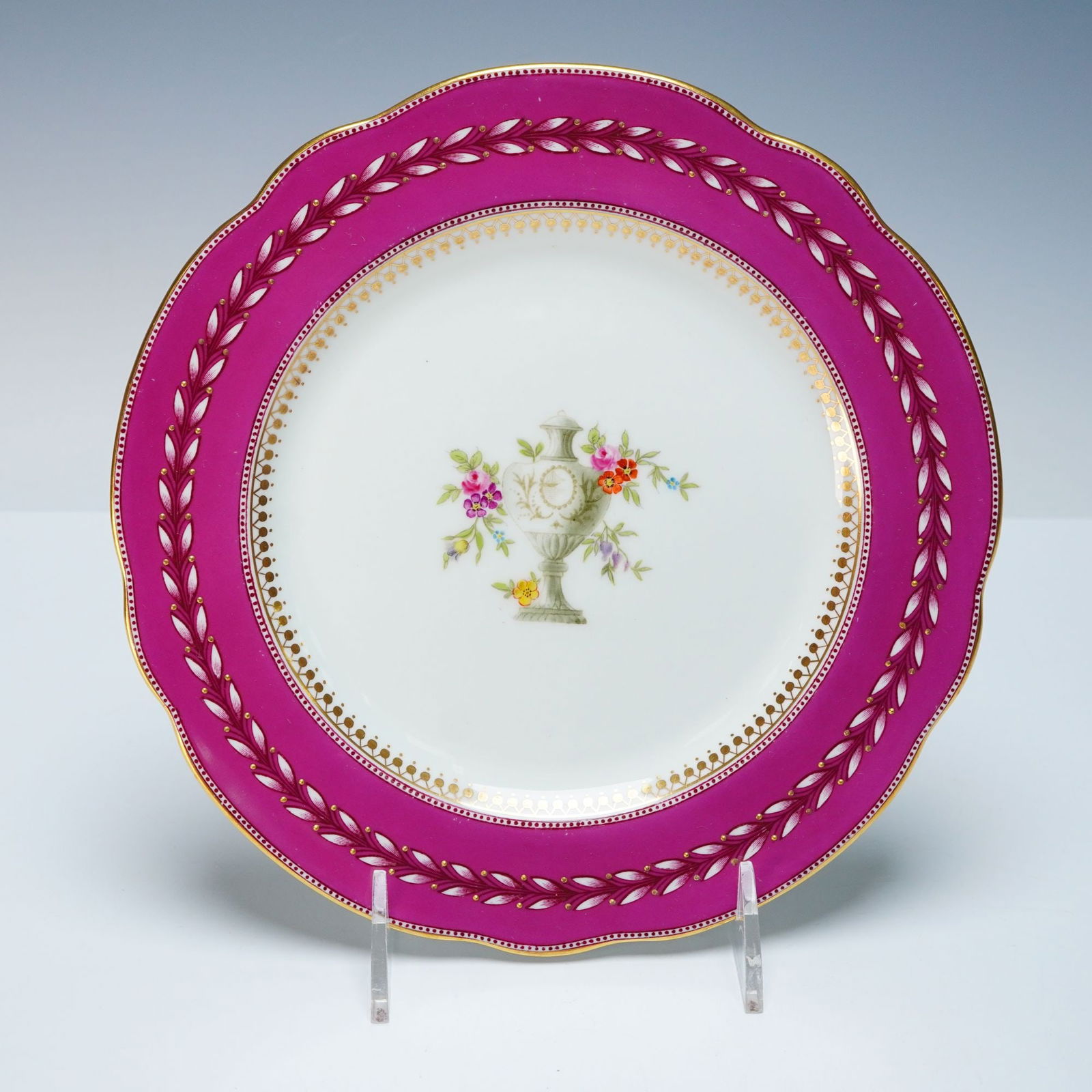 Wedgwood Porcelain Plate with Magenta Border and Gilt Urn Motif: A Wedgwood porcelain plate, circa 1910, featuring a scalloped rim and a vibrant magenta border embellished with intricate gilt leaf-and-berry motifs, framing a delicate dotted gilt inner band. The whi