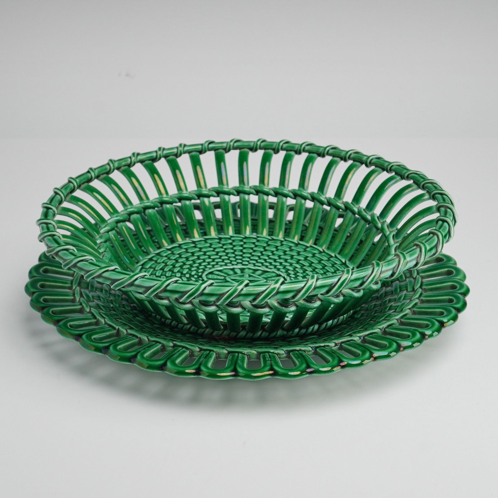 2pc Wedgwood Green Glaze Basketweave Bowl and Oval Plate: Wedgwood green glazed majolica ceramic basket and coordinating oval undertray. Both pieces feature a molded basketweave pattern with a central molded rosette motif on the interior. The basket is const