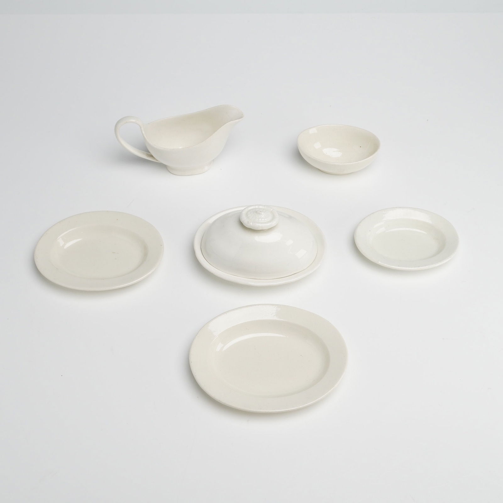6pc Wedgwood White Ceramic Tableware Collection: This 6pc collection of Wedgwood White ceramic tableware features a simple, undecorated design with a glossy cream-colored finish. The set includes a small covered dish with a knobbed lid, three oval d