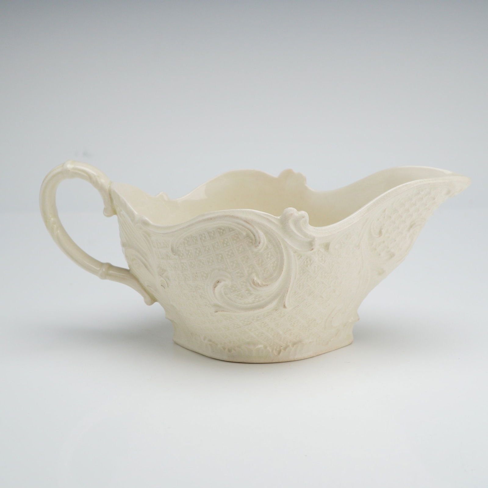 Wedgwood Salt-Glazed Stoneware Sauce Boat: This press-molded white salt-glazed stoneware sauce boat, likely produced in Staffordshire, England, dates to the mid-18th century. The vessel features intricate relief-molded decoration, including pa