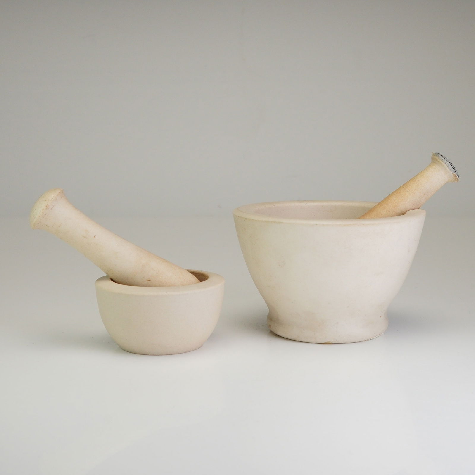 Set of 2 Wedgwood Mortars and Pestles: A set of two Wedgwood mortar and pestle sets, totaling four items, crafted from matte off-white biscuit porcelain. The collection includes mortars of two different sizes with their corresponding pestl