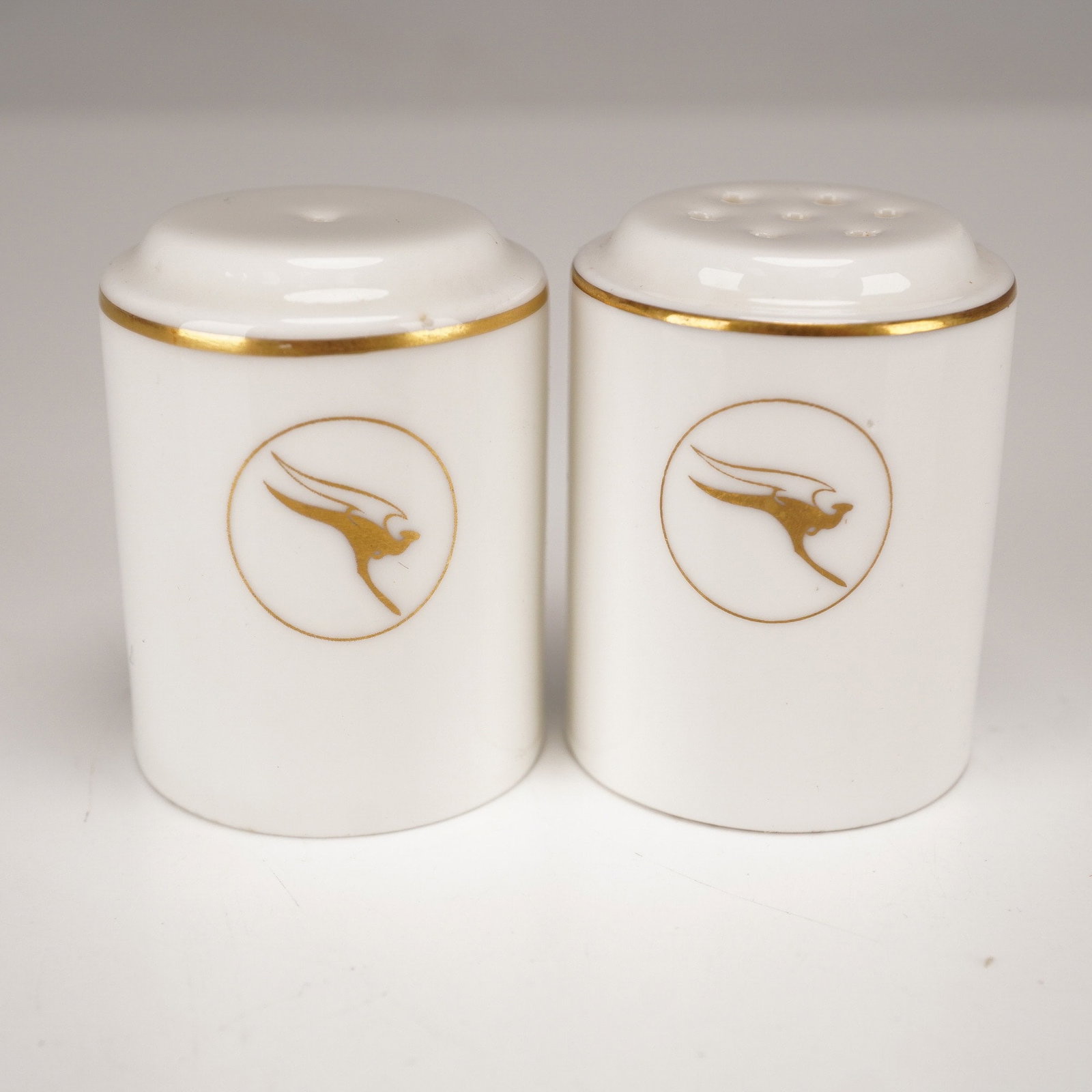 Wedgwood Salt & Pepper Shakers for Qantas Airways Airlines: Each white cylindrical shaker features a thin gilt band at the upper rim and displays the Qantas "Flying Kangaroo" logo in gilt. The undersides are marked "Wedgwood, Made in England." Collection stick