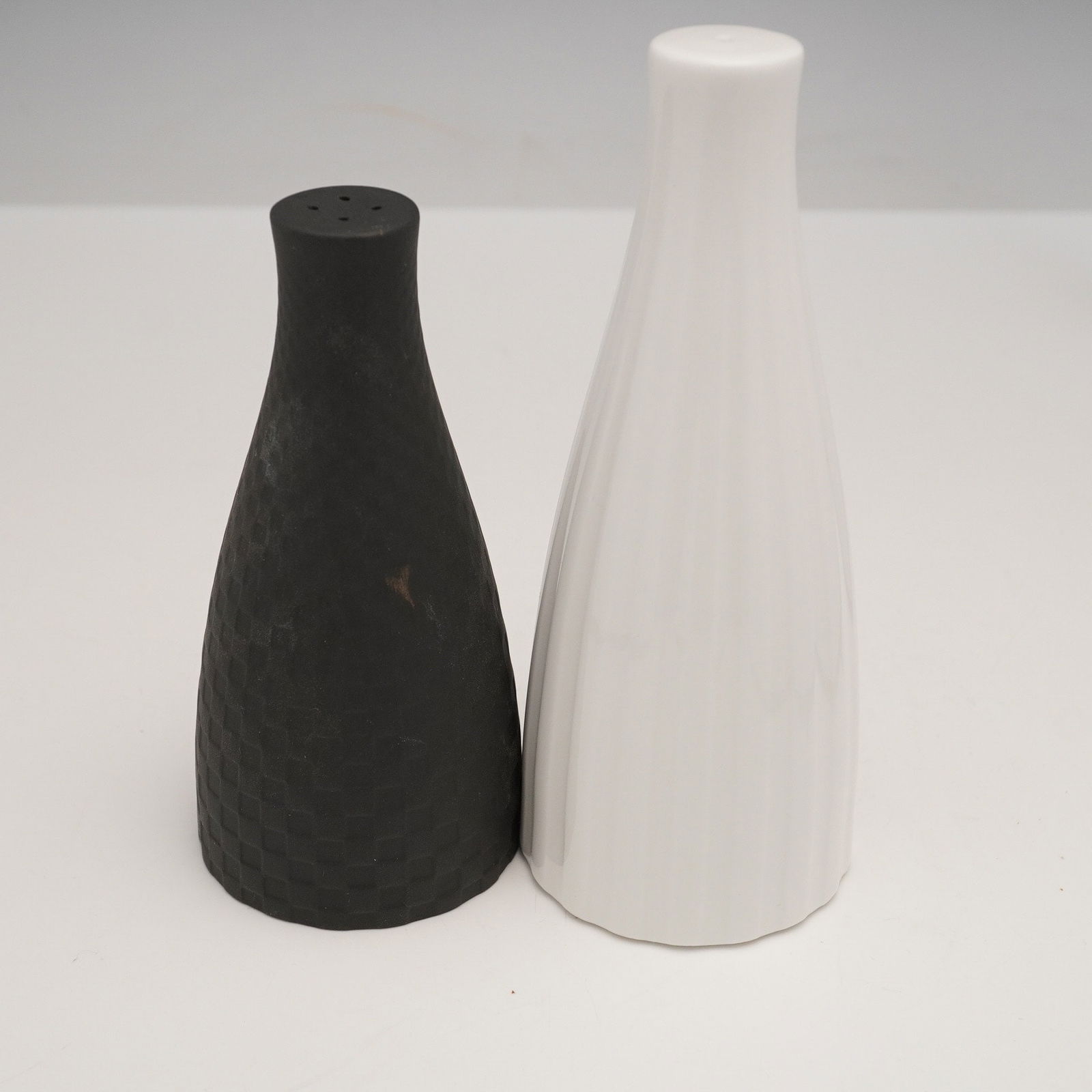 A Pair of Wedgwood 'Night and Day' Salt and Pepper Shakers: A Pair of Wedgwood 'Night and Day' salt and pepper shakers. Each shaker features a tapered, conical form. One shaker is matte black with a finely textured, grid-like surface and three top holes, sugge