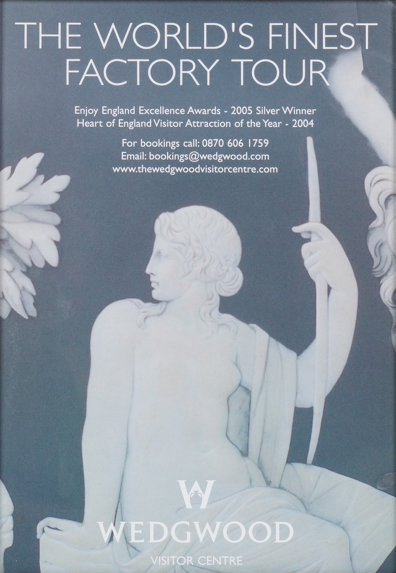 Framed Wedgwood Visitor Centre Factory Tour Advertisement Poster: A framed Wedgwood poster advertising "THE WORLD'S FINEST FACTORY TOUR," featuring a white classical figure in relief style against a dark grey background, set in a mat silver tone frame. DimensionsFra