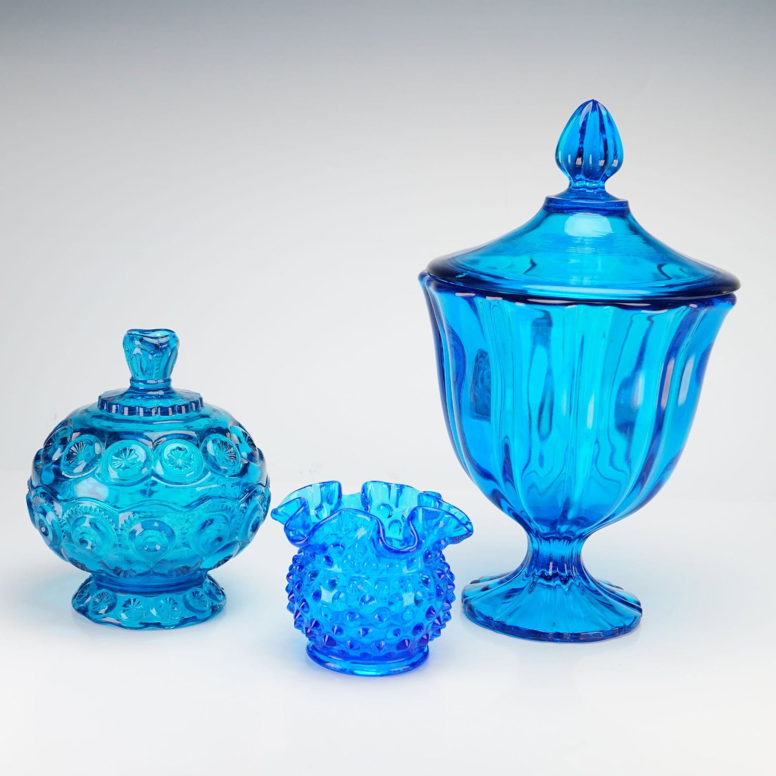 L.E. Smith and Fenton Peacock Blue Glass Moon and Star and Hobnail Collection: This lot consists of three pieces of mid-century American pressed art glass in vibrant shades of blue. Included is an L.E. Smith Moon and Star lidded candy dish in peacock blue, featuring the classic