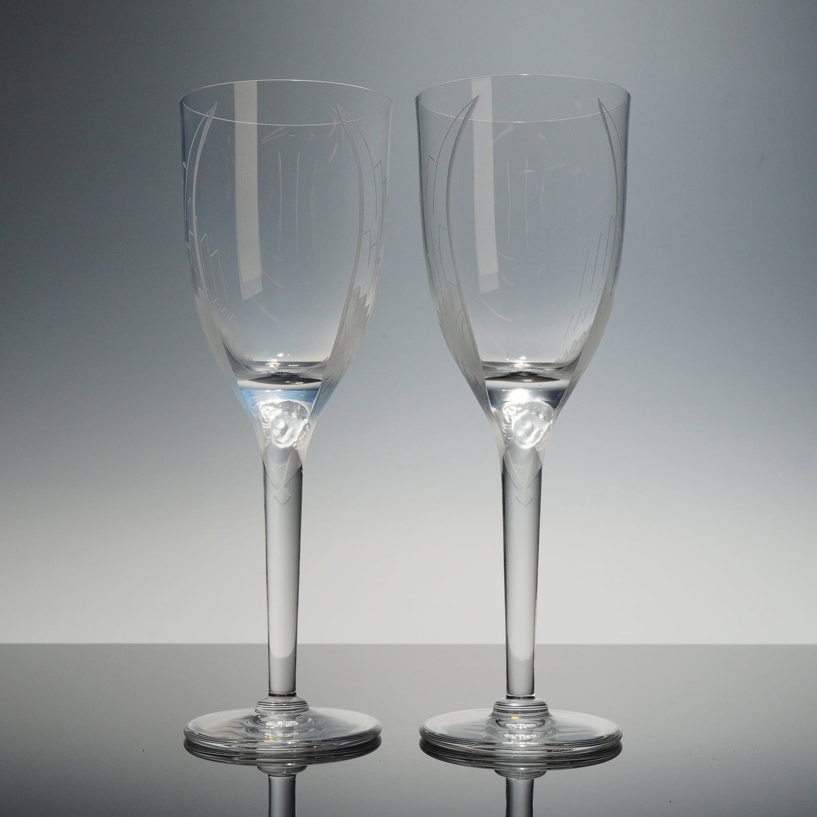 Pair of Lalique Ange Crystal Champagne Flutes: A pair of fine lead crystal champagne flutes in the "Ange" (Angel) pattern by Lalique. The design features clear bowls with delicate, vertically etched wings. The upper portion of the stem is adorned