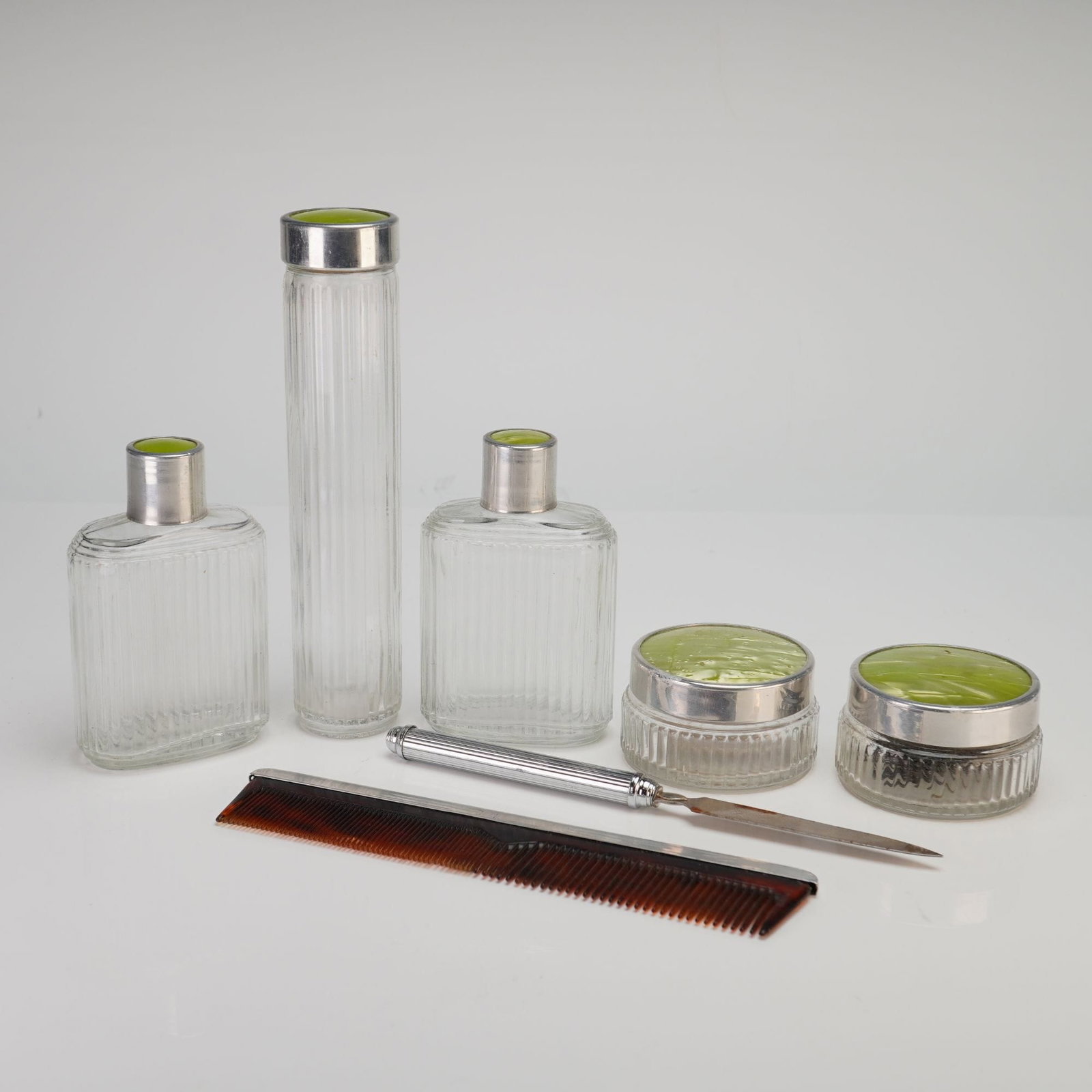 Art Deco 5pc Enamel and Glass Vanity Set with Green Guilloche: This Art Deco 5pc enamel and glass vanity set is a coordinated collection of dressing table accessories featuring vertically fluted clear glass and silver-toned metal hardware. The assembly includes a