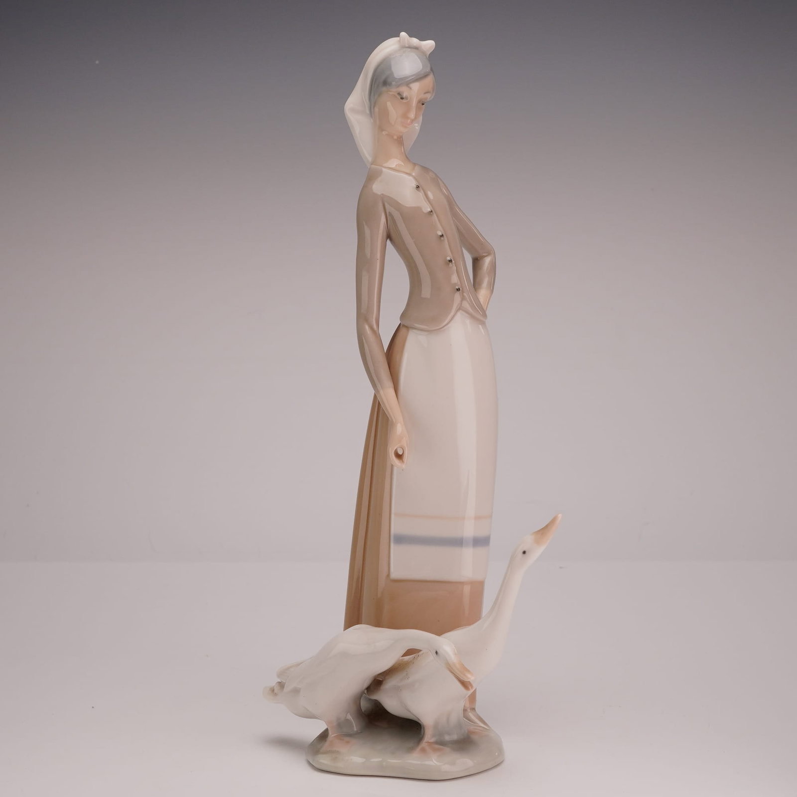 Lladró Porcelain Figurine, Girl with Geese 01001035: A Lladró glazed porcelain figurine titled Girl with Geese (model #01001035). This piece depicts a young woman in a stylized, elongated form characteristic of the mid-period Lladró aesthetic. She is