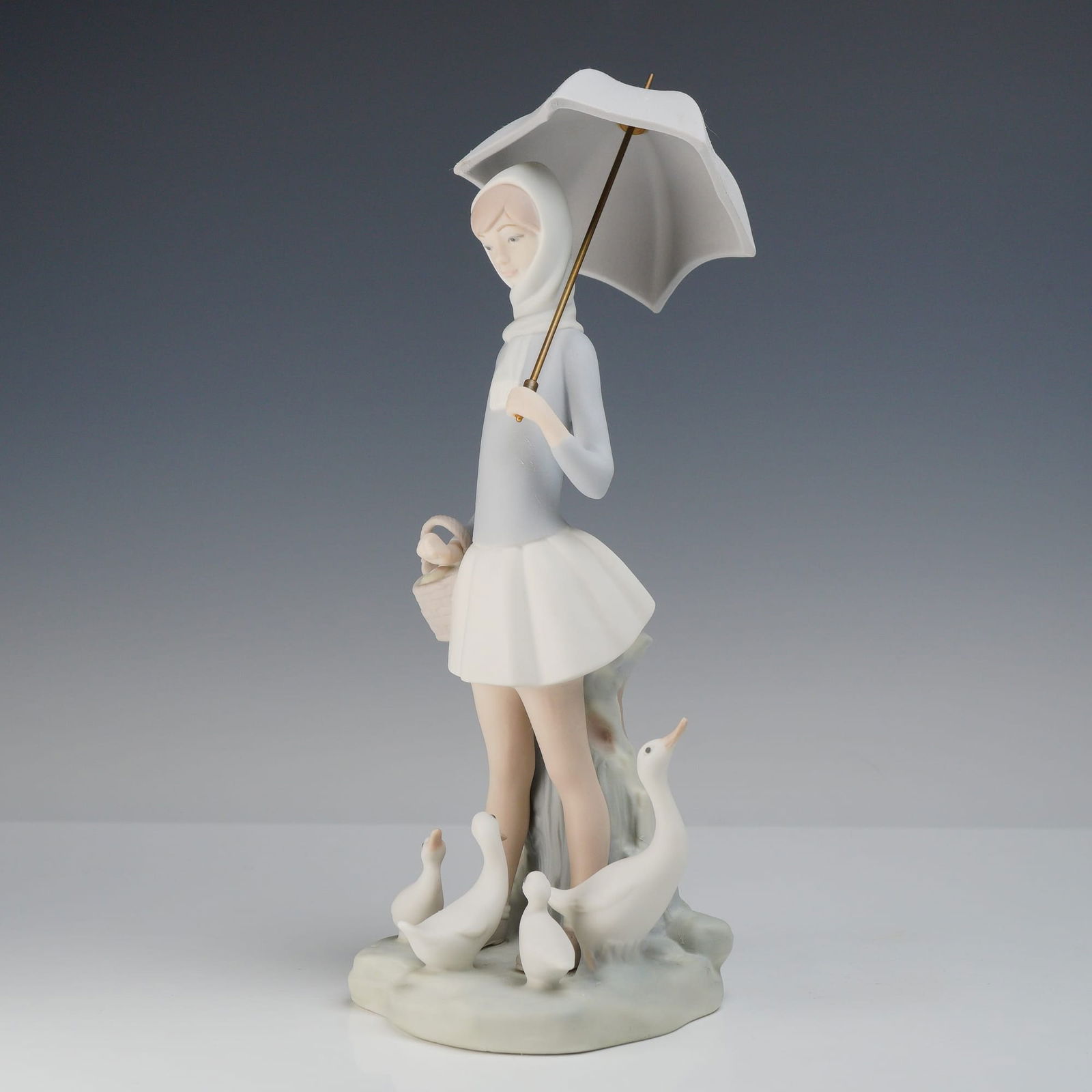 Lladro Girl with Umbrella and Geese Matte Porcelain Figurine 4510: Lladro matte porcelain figurine titled Girl with Umbrella and Geese, model number 4510. The figurine depicts a young woman dressed in a light gray long-sleeved hooded top and a short white pleated ski
