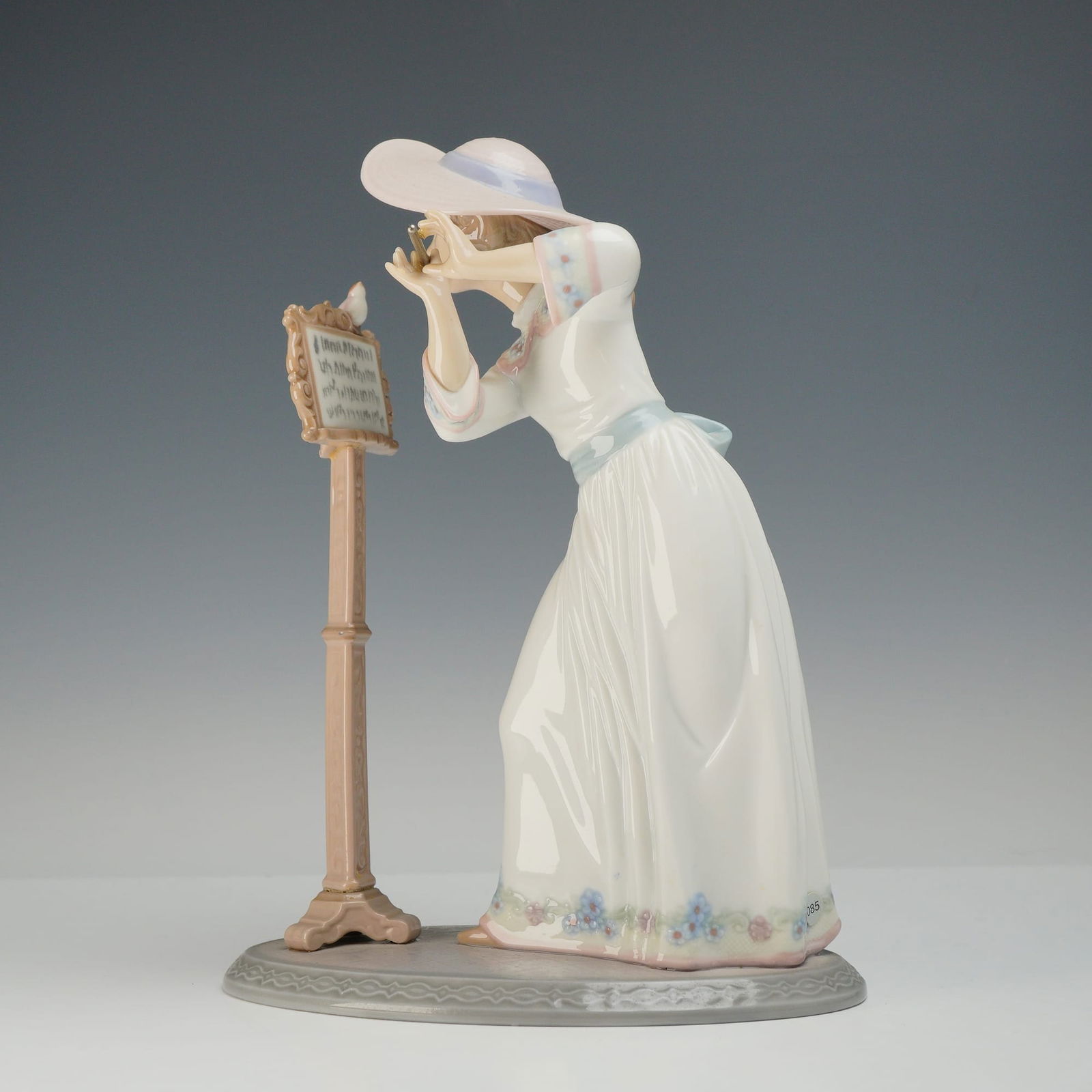Lladro Porcelain Figurine Songbird 6093: This Lladro porcelain figurine is identified as Songbird model number 6093. The piece depicts a young woman in a late 19th-century style white gown featuring a blue sash and floral embroidery along th