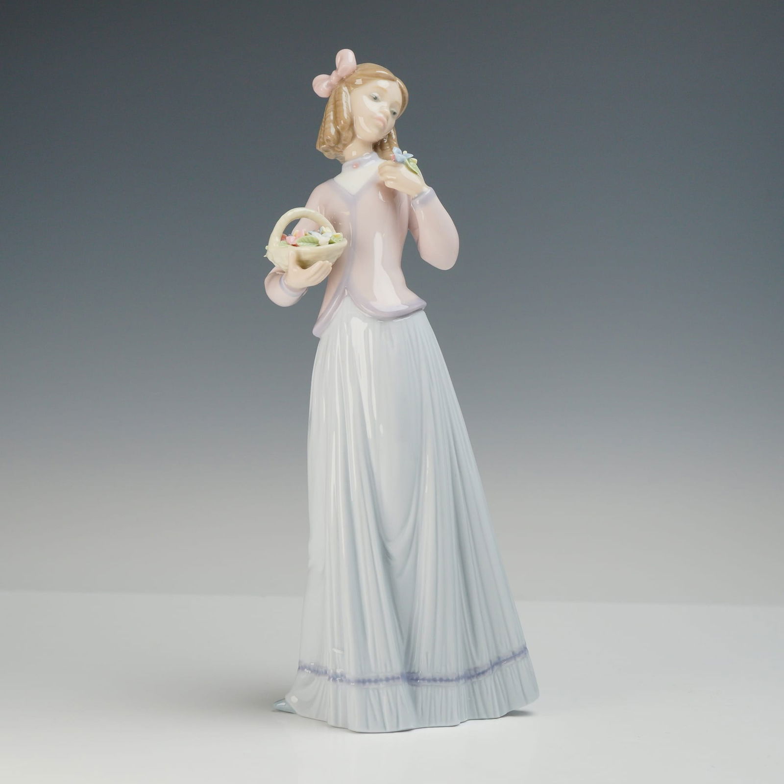 Lladro Porcelain Figurine Innocence in Bloom Number 7644: A Lladro polychrome glazed porcelain figurine titled Innocence in Bloom, model number 7644. The figure depicts a young woman in a standing pose, dressed in a pale pink jacket over a long, light blue s