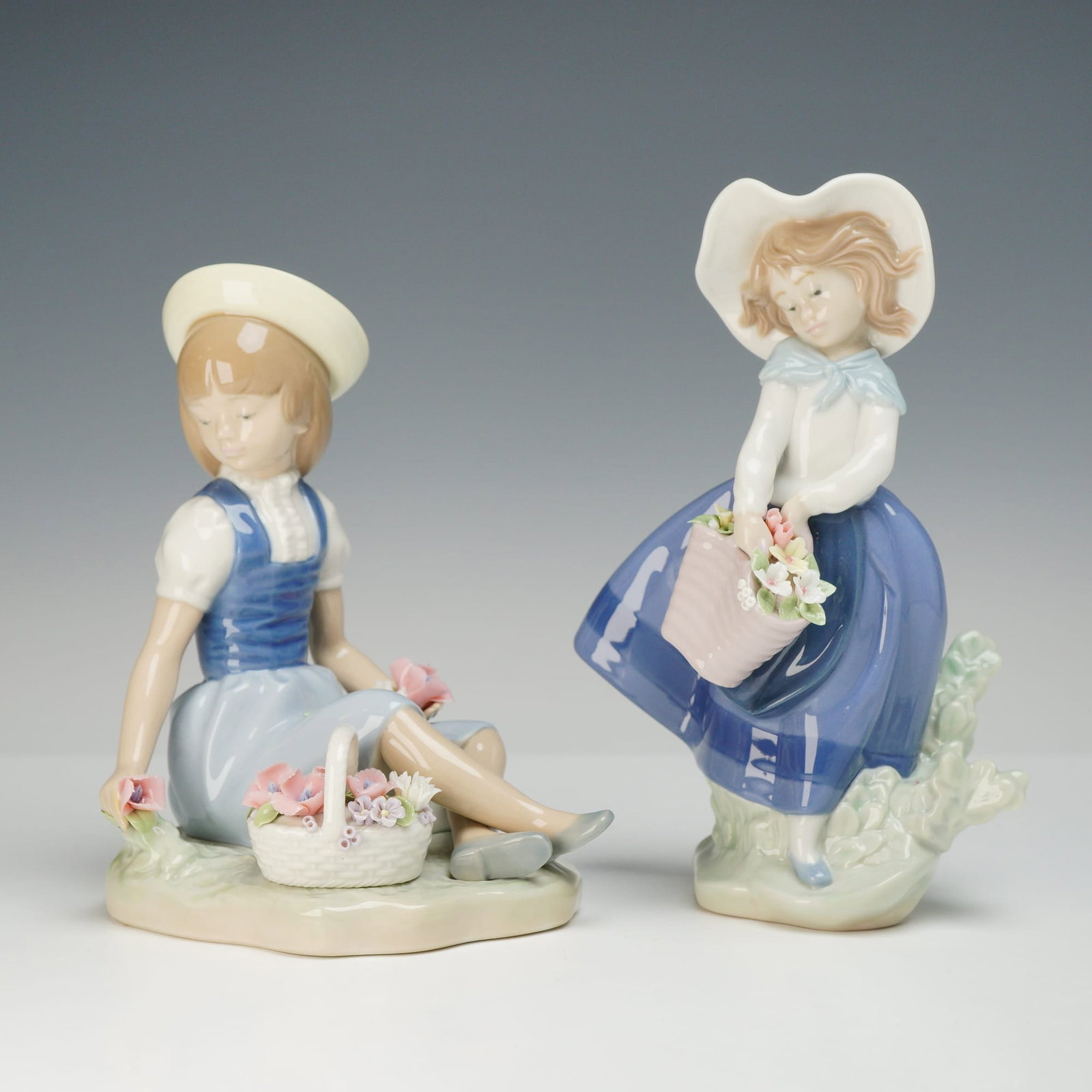 Two Lladró Porcelain Figurines, Picking Flowers & Pretty Pickings: This lot consists of two glazed porcelain figurines manufactured by Lladró in Spain. The first figurine, titled Picking Flowers (model number 1287), depicts a seated girl wearing a blue and white dre