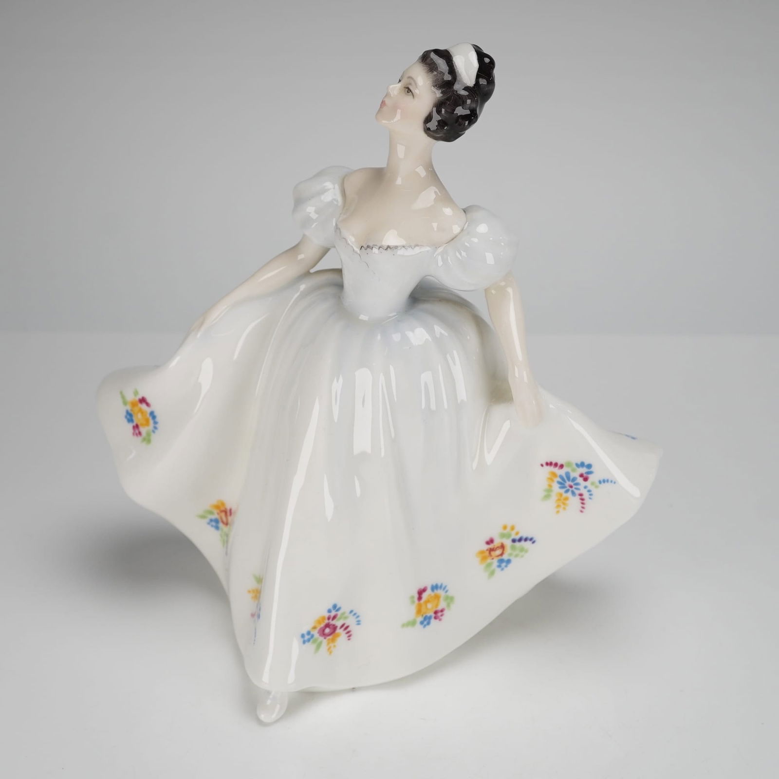 Royal Doulton Figurine Kate HN 2789: The piece depicts a young woman in a dynamic, full-skirted pose, consistent with the identified Royal Doulton Figurine model. She wears a high-gloss white gown with large, puffed sleeves and a wide, f