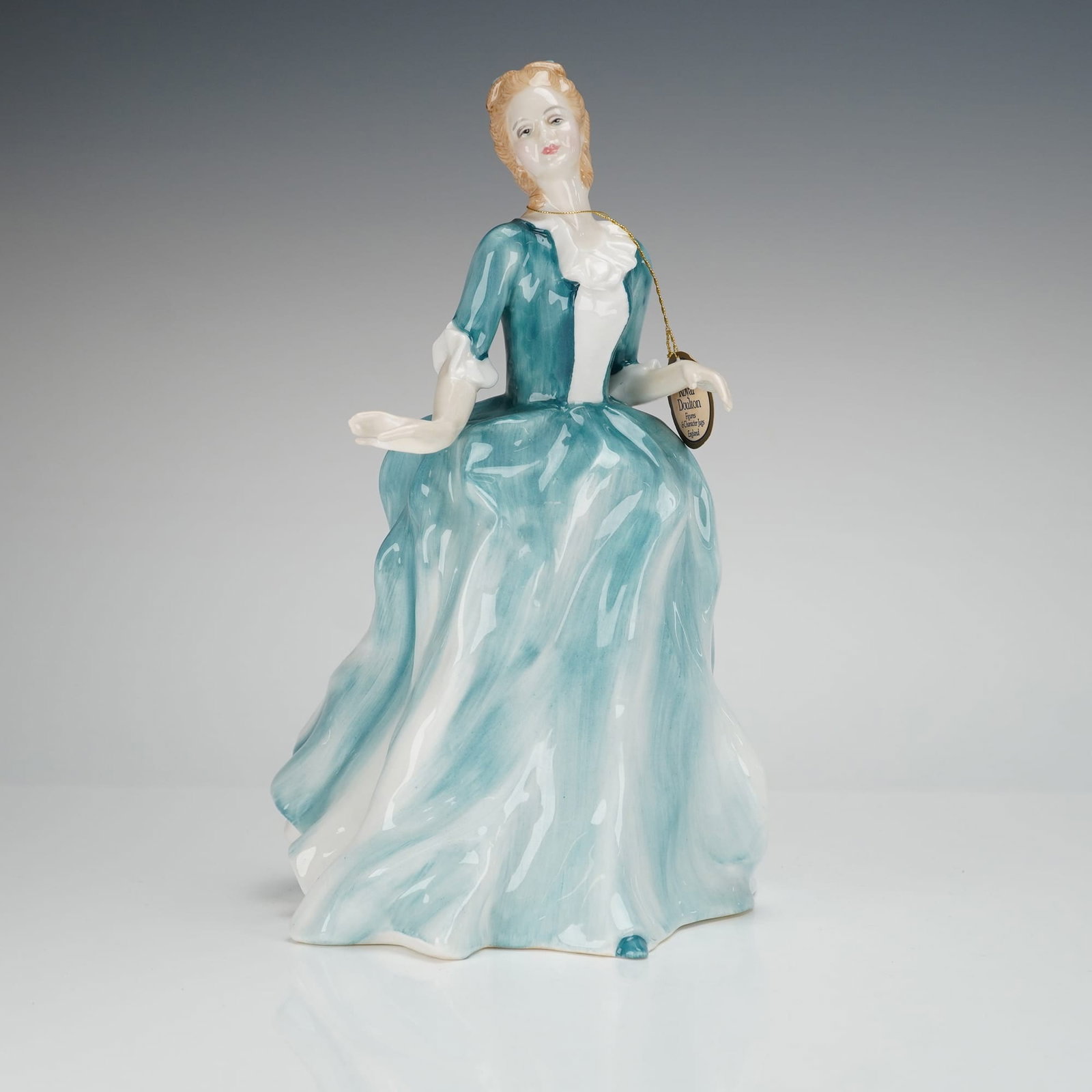 Royal Doulton Figurine Yvonne HN3038: The figure was designed by Adrian Hughes and copyrighted in 1988. The standing woman is depicted wearing a voluminous period gown featuring flowing teal blue and white coloration. The item retains its
