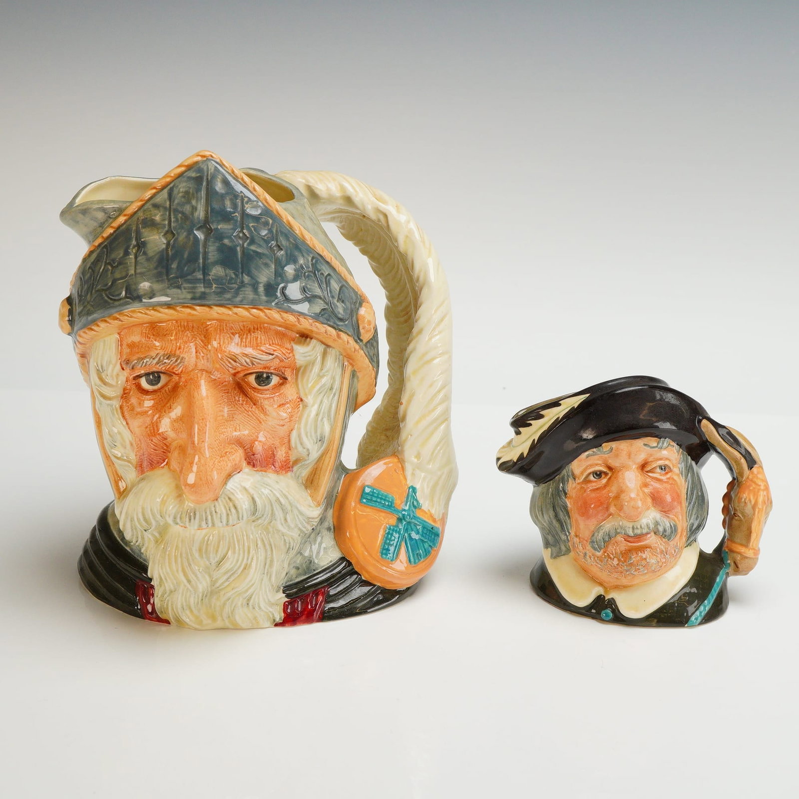 2pc Royal Doulton Character Jugs, Don Quixote and Sancho Panca: This pair of Royal Doulton ceramic character jugs, dated 1956, depicts the literary figures Don Quixote and his squire, Sancho Panca. The larger Don Quixote jug, model D 6455, features a weathered fac