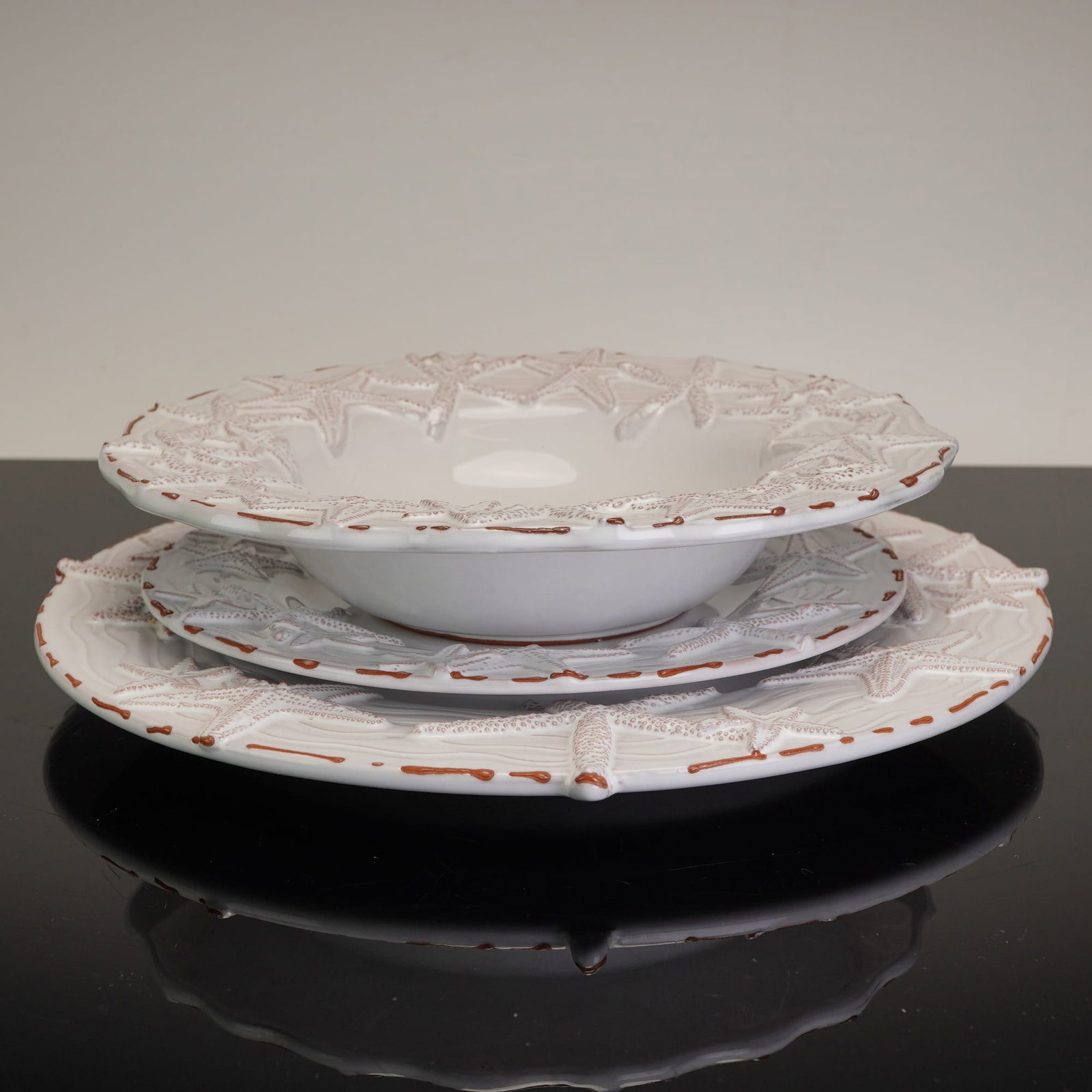 Mud Pie Starfish Three-Piece Ceramic Place Setting: This three-piece ceramic place setting by Mud Pie features a coastal nautical theme in the Starfish pattern. The set is crafted from earthenware with a visible reddish-brown terracotta foot rim and fi